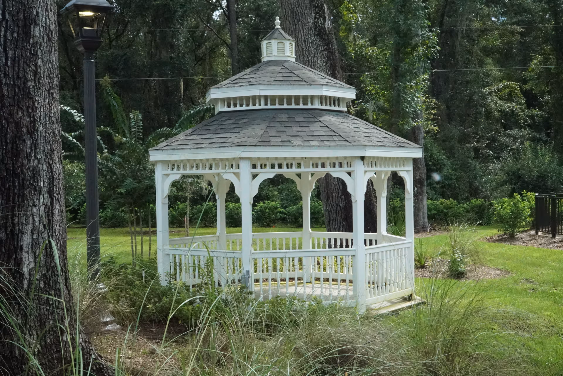 White gazebo on a manicured lawn surrounded by trees in a peaceful garden.