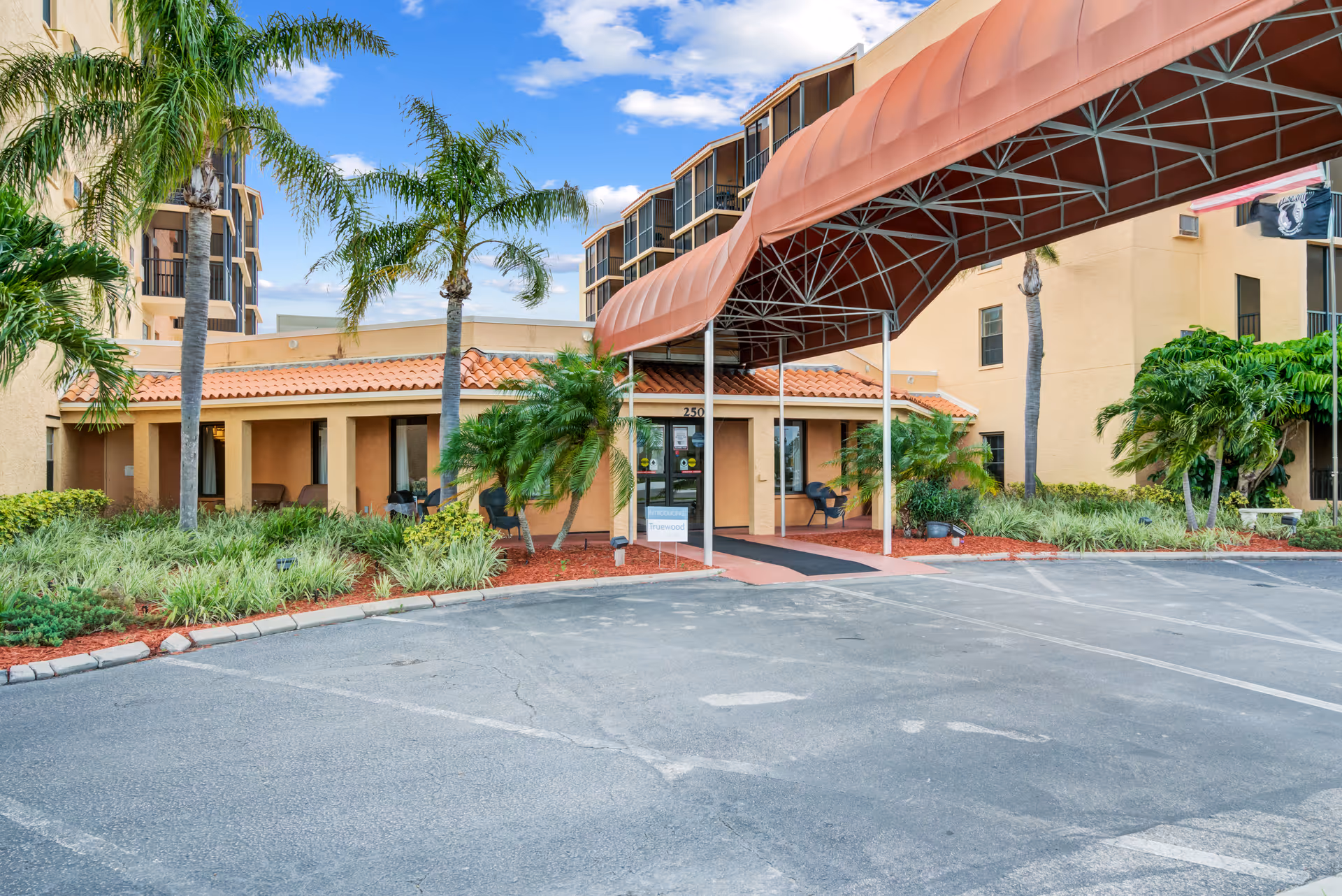 Exterior view of a senior living facility entrance with a curved covered awning and landscaping.