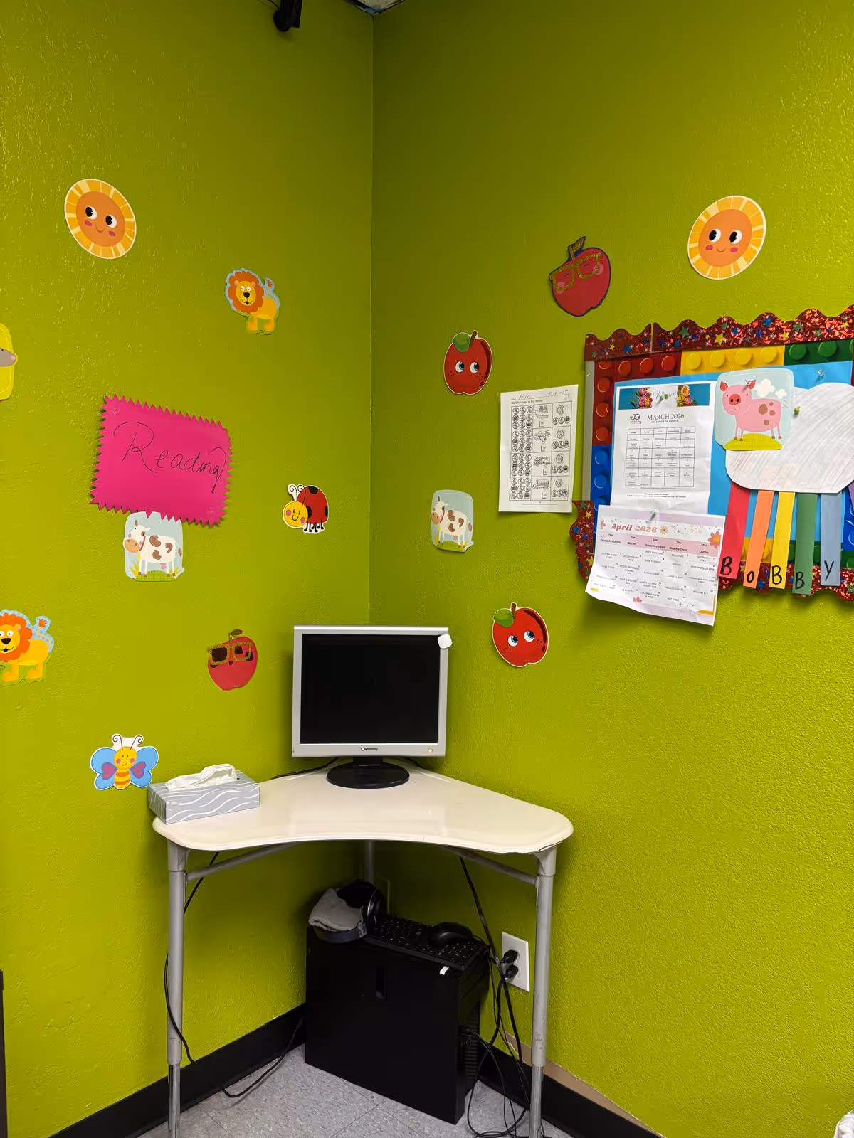 Bright lime-green corner with a small desk, computer monitor, and colorful wall decorations.