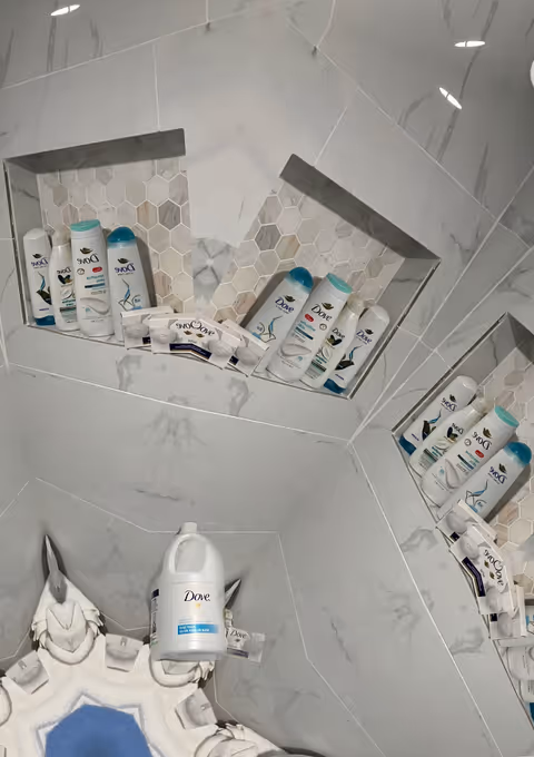 Built-in tiled shower with Dove toiletries arranged in recessed wall niches.