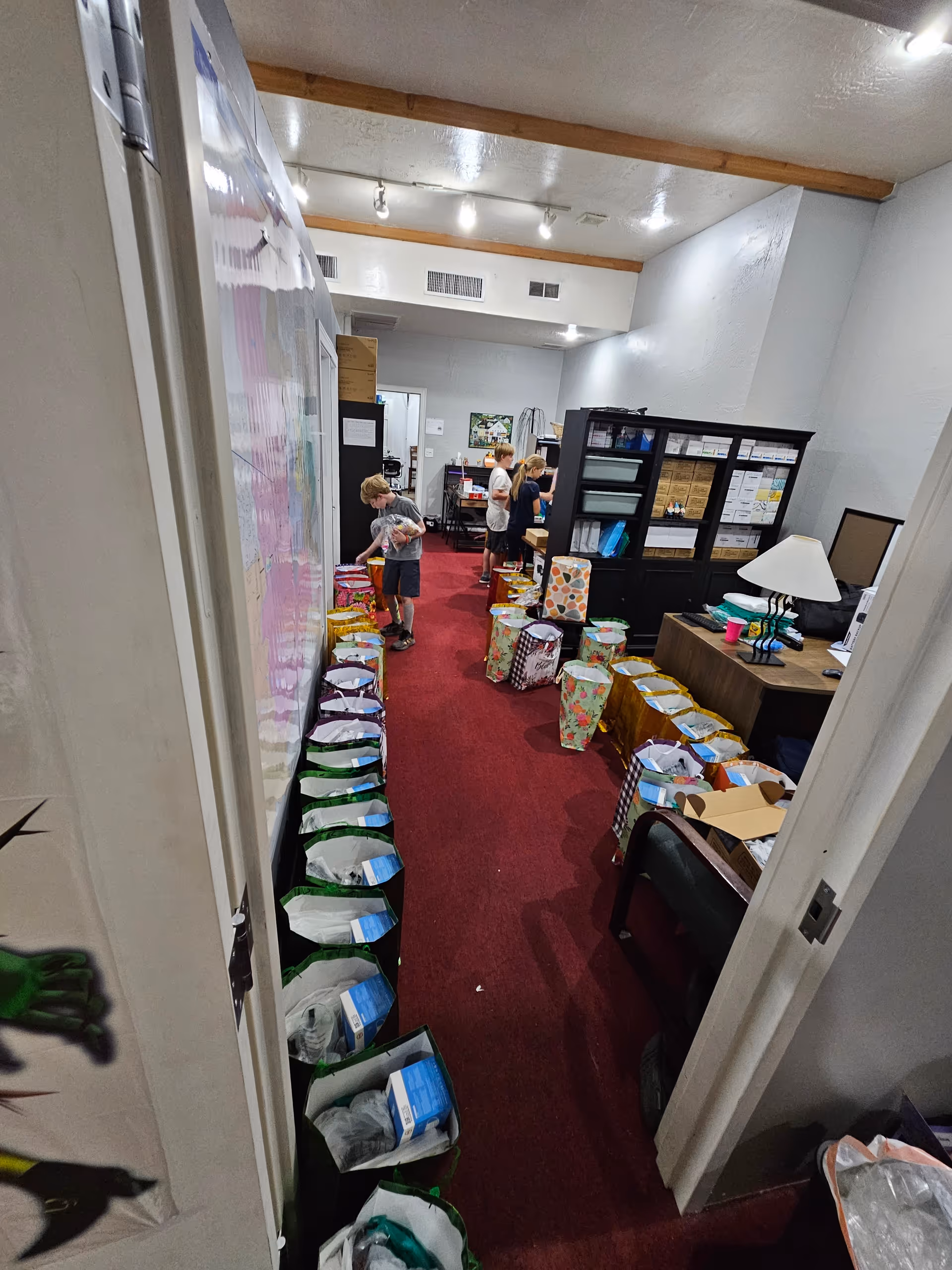 Hallway in a senior living facility with staff organizing colorful bags along a red carpet.