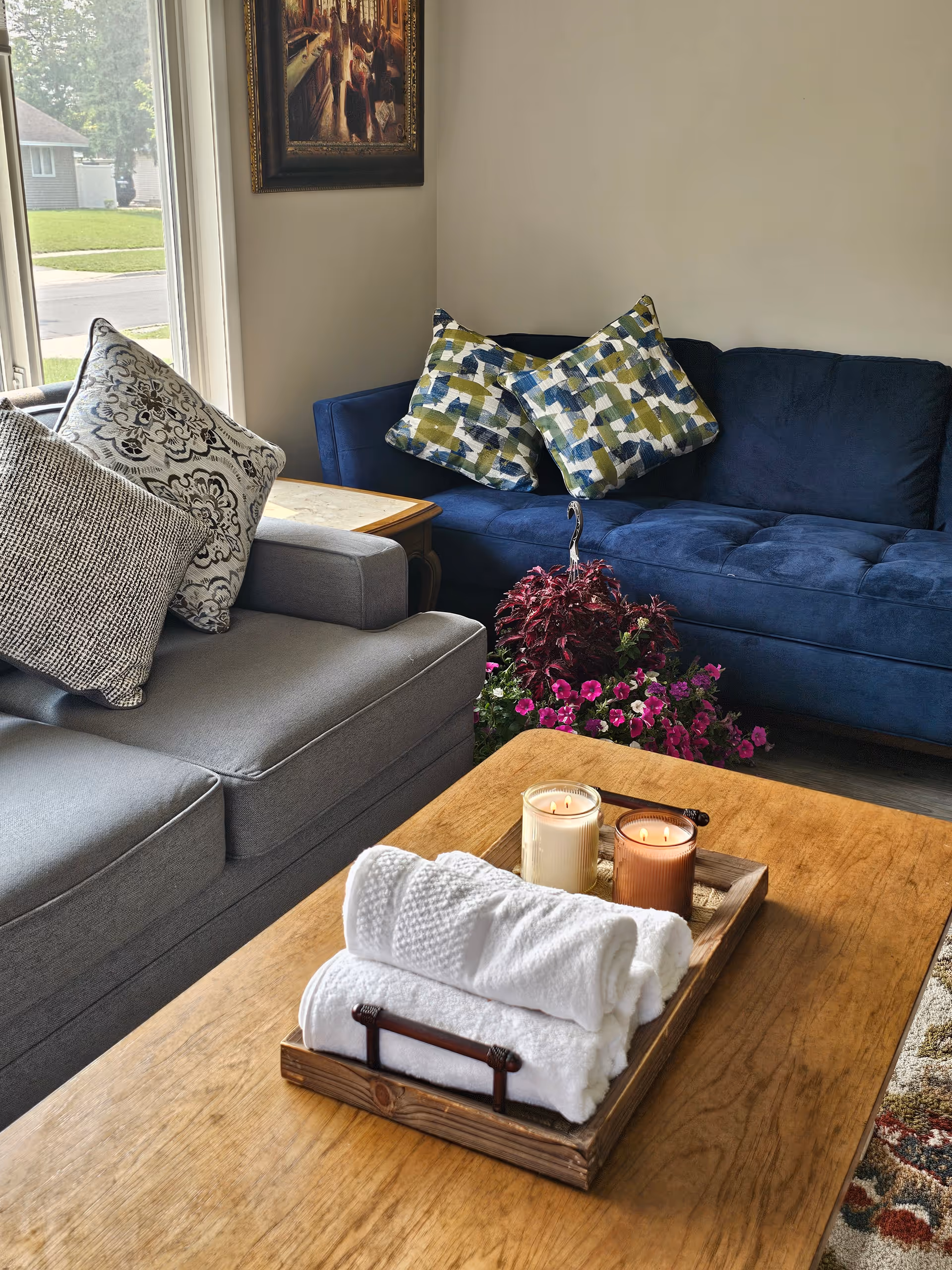 Cozy living room with a blue sofa, patterned pillows, flowers, and a wooden coffee table.
