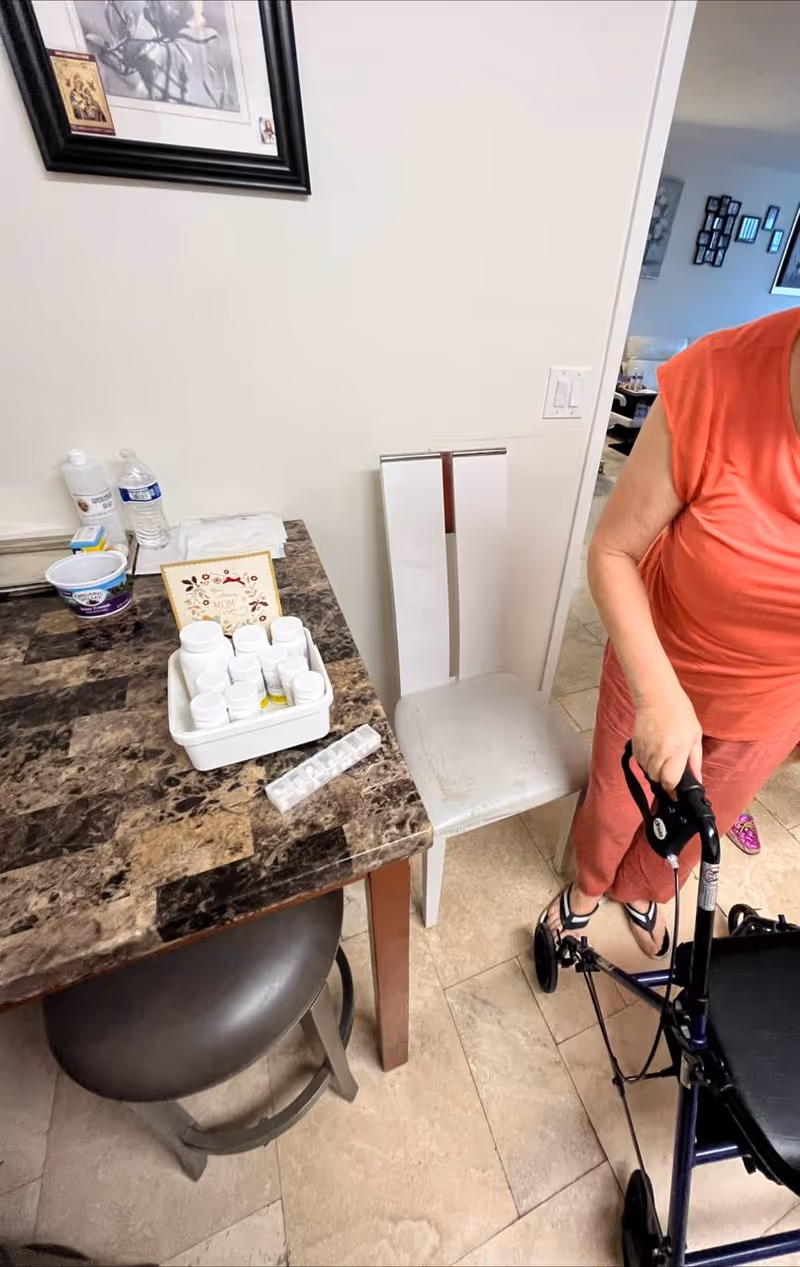 A kitchen counter with medication bottles, a pill organizer, and a walker beside a person.