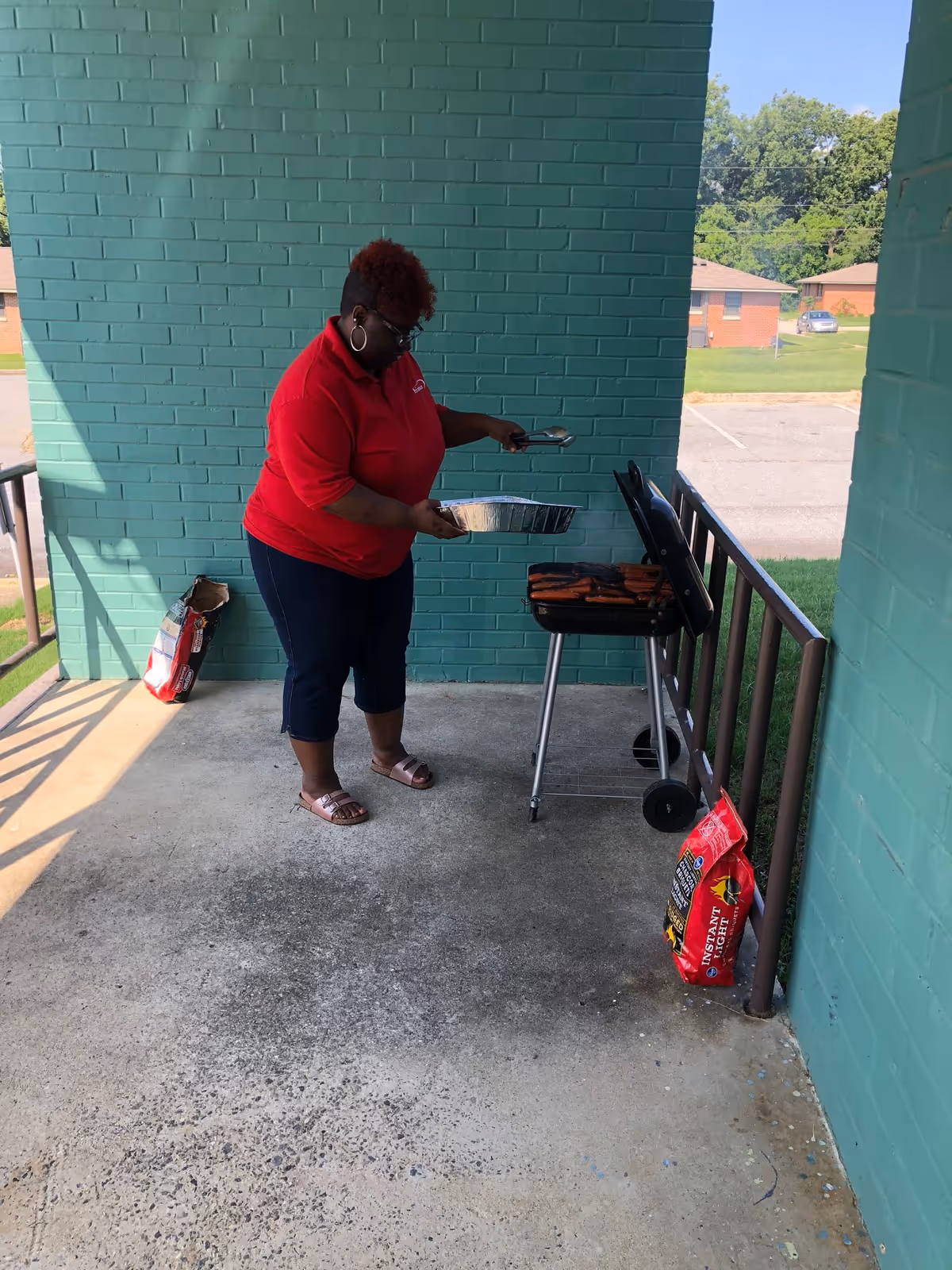 A person grills on an outdoor patio beside teal brick walls.
