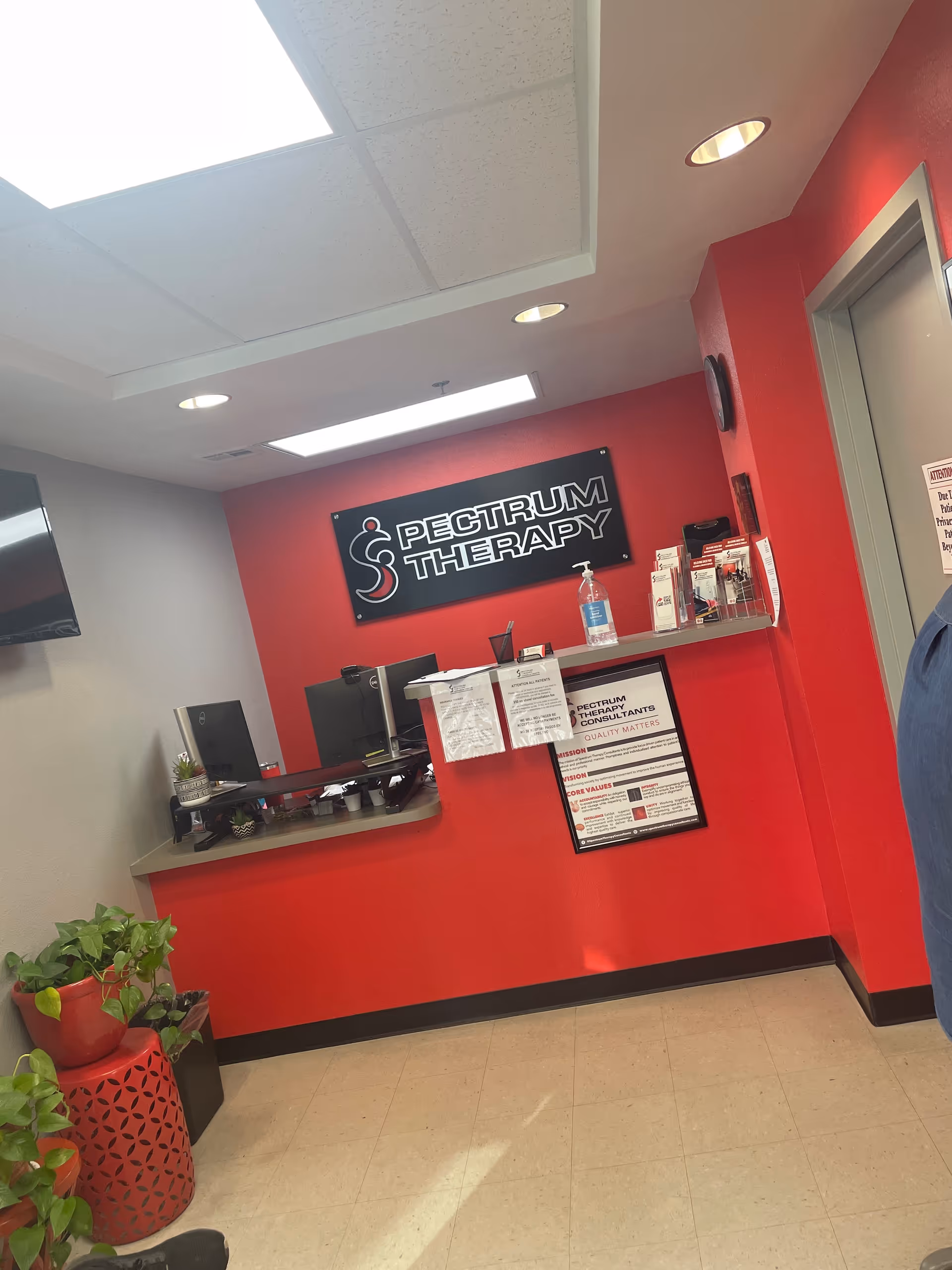 Reception area with red wall, Spectrum Therapy sign, desk, and plants.