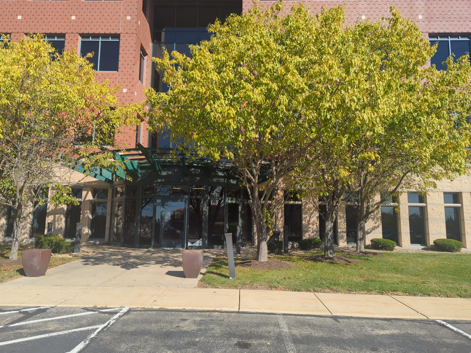 Front exterior of a brick Heartland Hospice building with glass doors and trees.