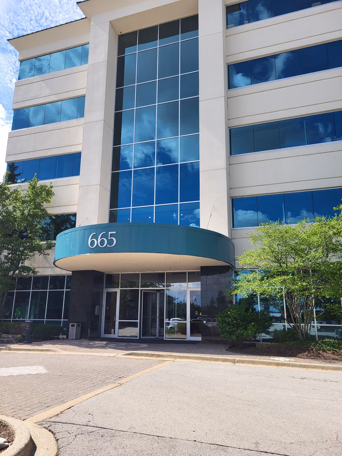 Modern building exterior with tall glass windows and a teal curved entrance canopy.
