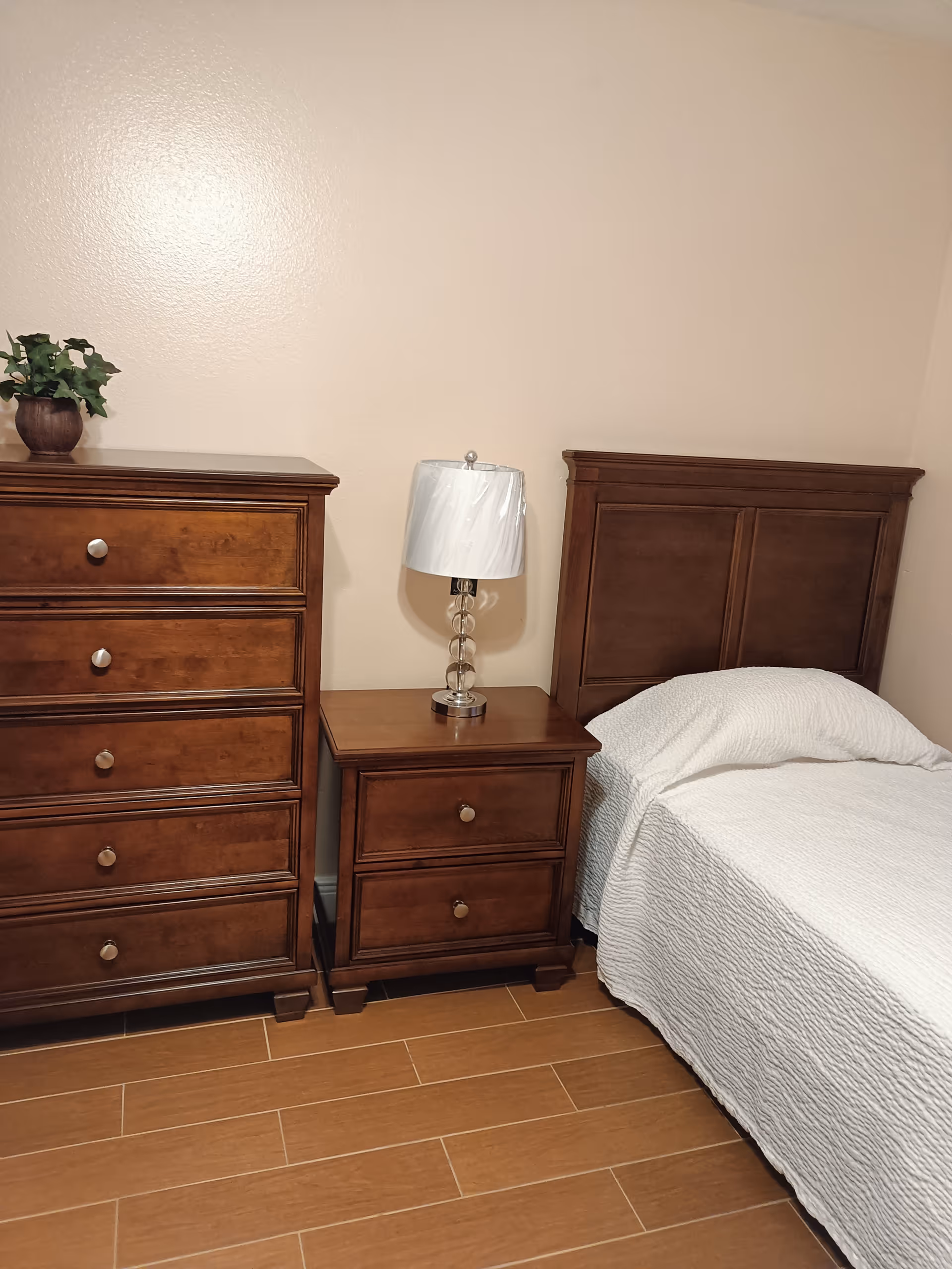 Wooden bedroom featuring a bed, nightstand, dresser, lamp, and potted plant.