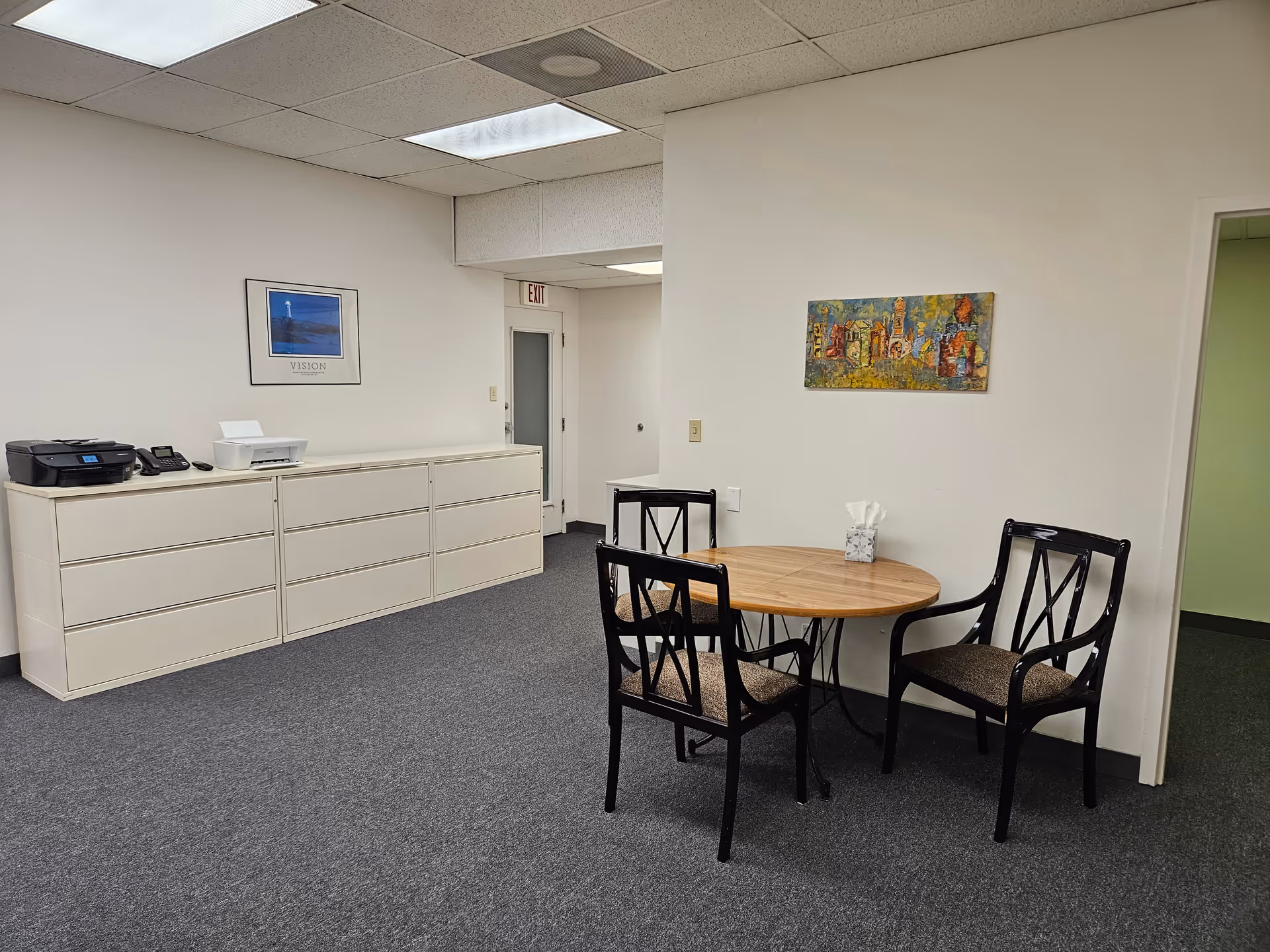 White walls, round table with chairs, and a long cream cabinet in a waiting area.