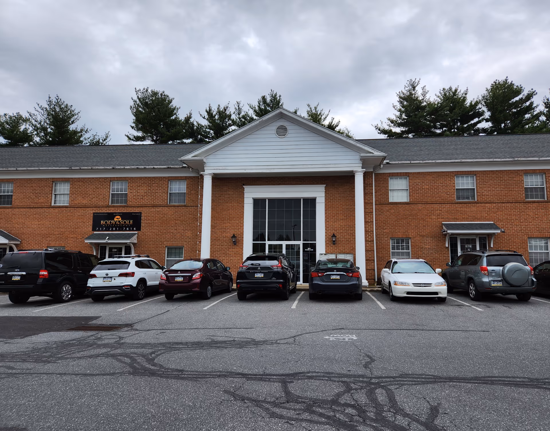 Brick office building with a central entrance and a row of parked cars in front.