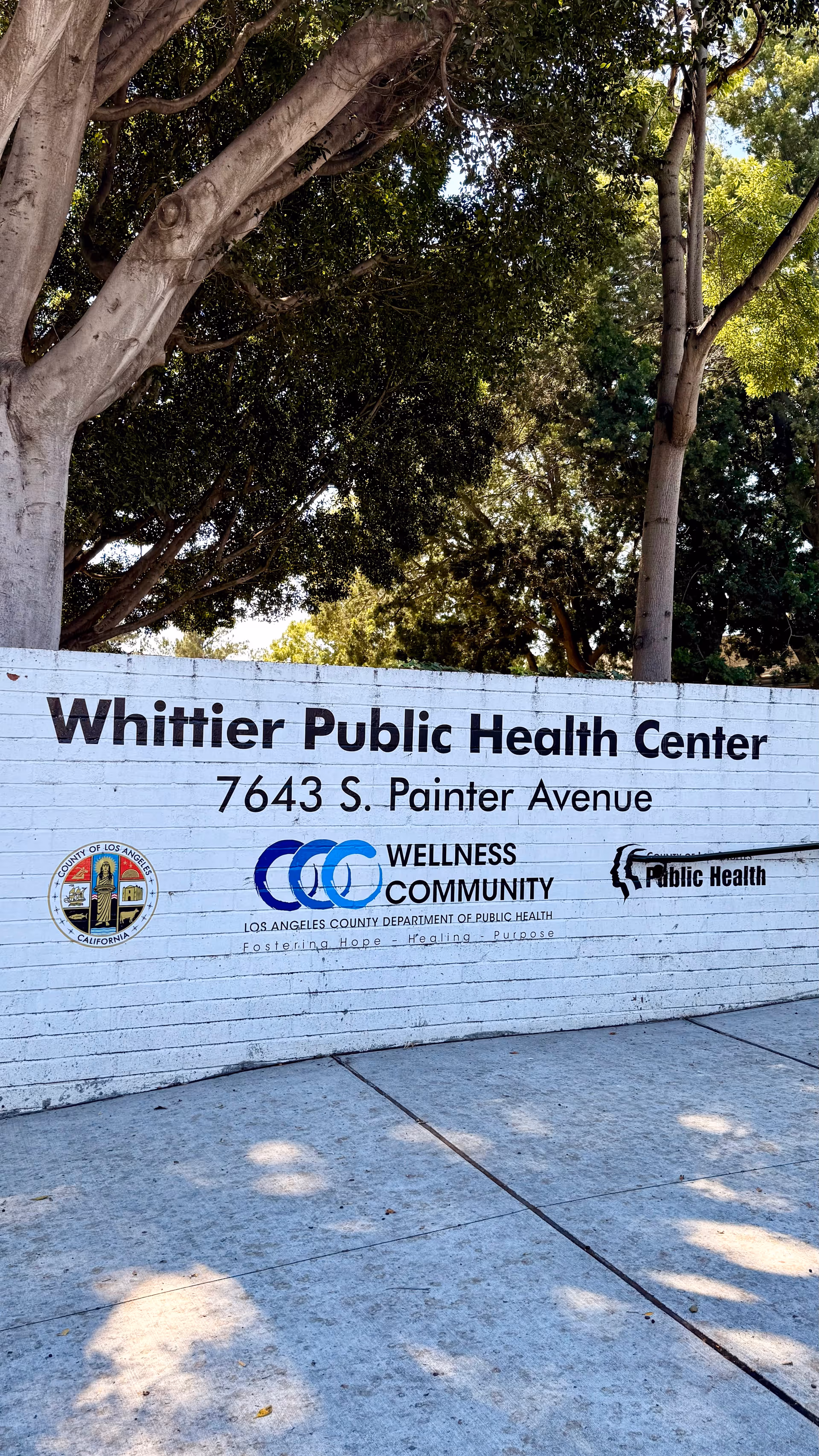 Exterior sign reads Whittier Public Health Center with trees behind.