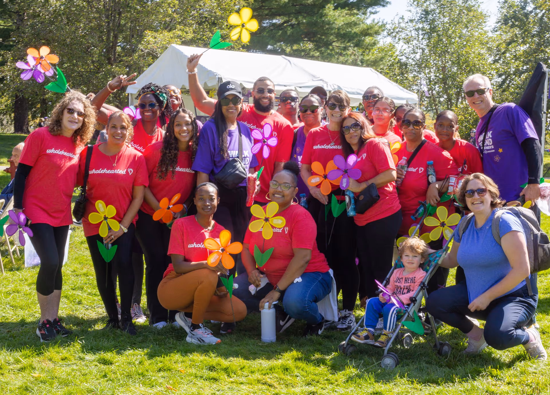 A group of volunteers is posing outdoors with colorful pinwheel flowers and tents.
