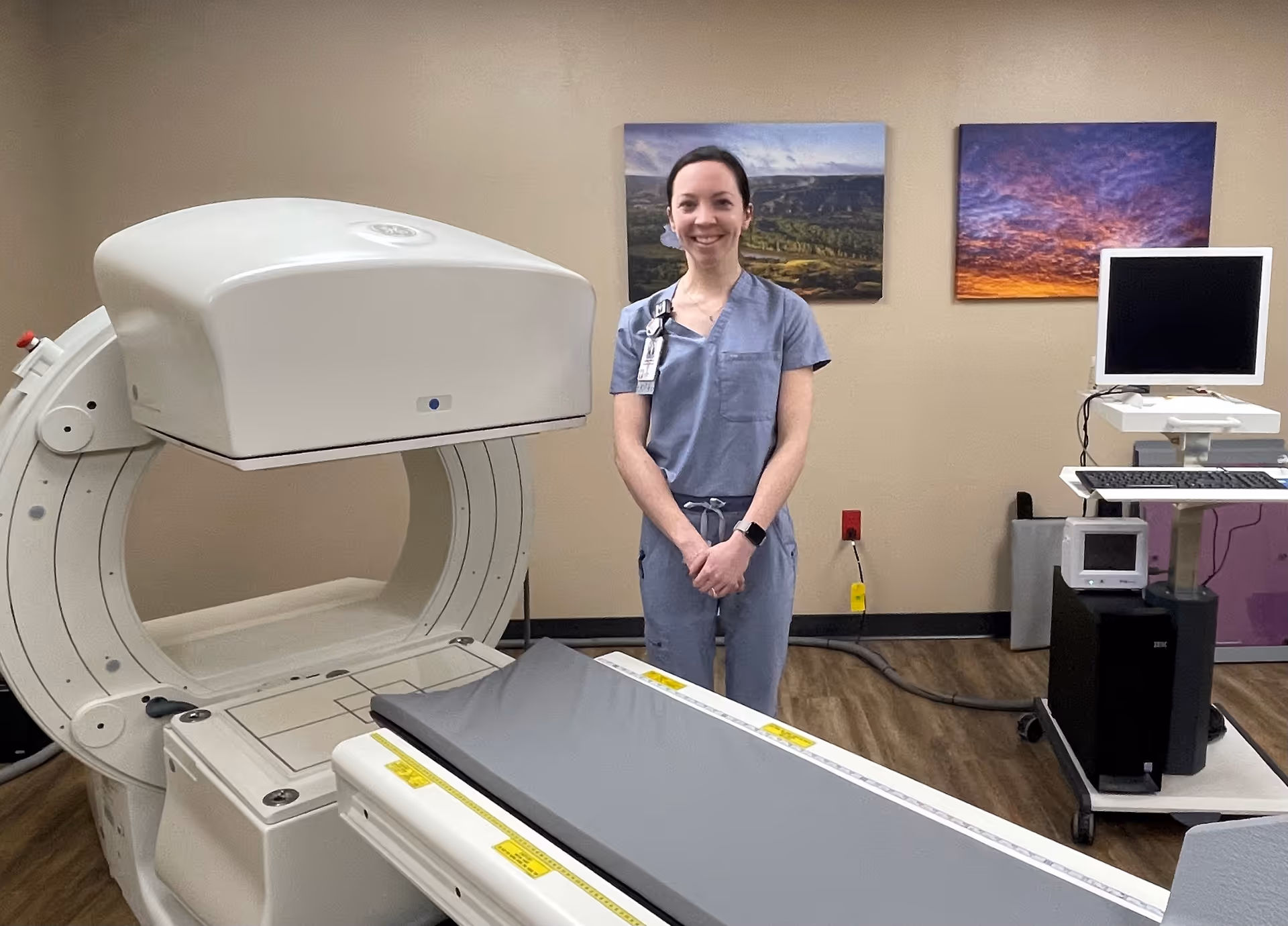A medical professional in scrubs stands beside an MRI scanner in a clinical room.