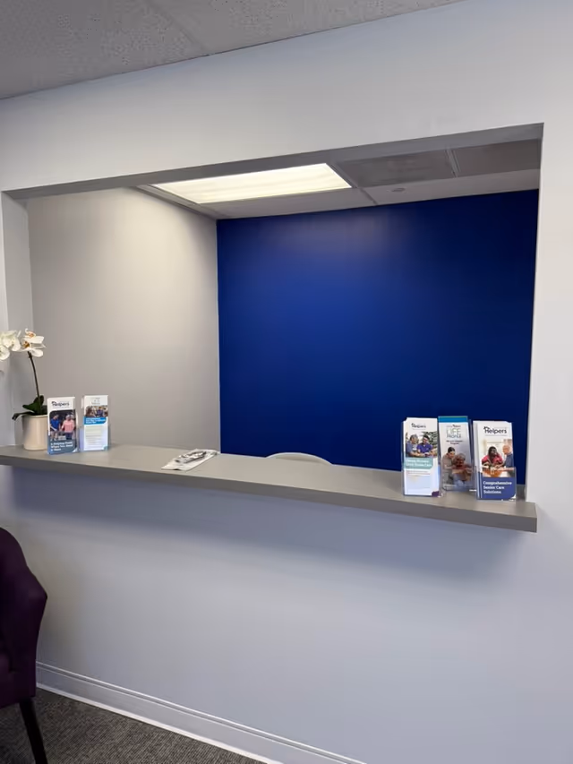 Reception desk with a blue wall, brochure stands, and a potted white orchid at Senior Helpers.