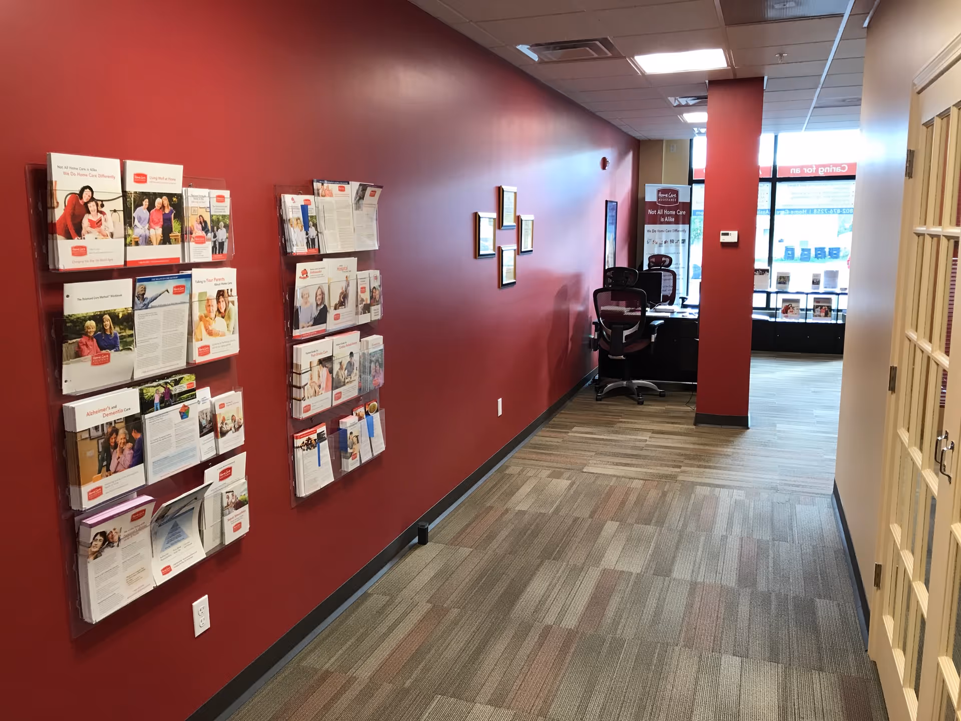 Red-walled hallway with brochure racks, framed pictures, and a small desk area in the distance.