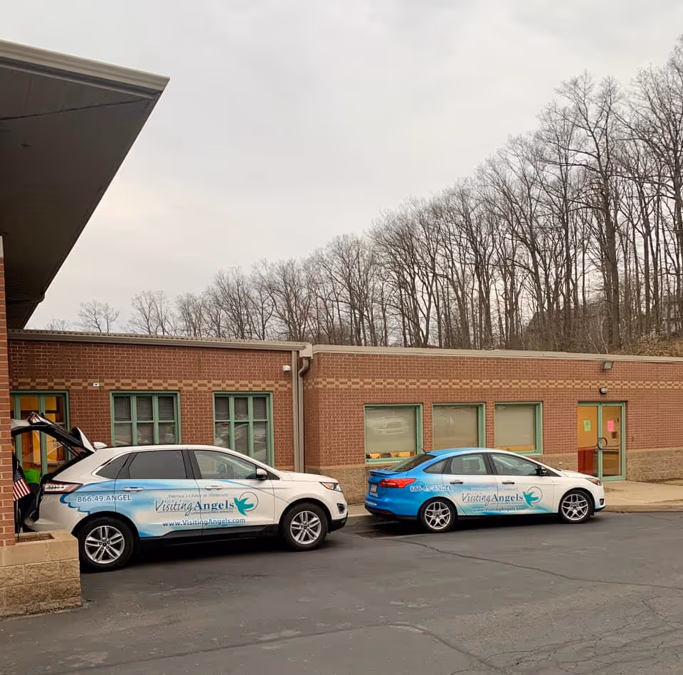 Two branded Visiting Angels cars parked in front of a brick senior care facility.