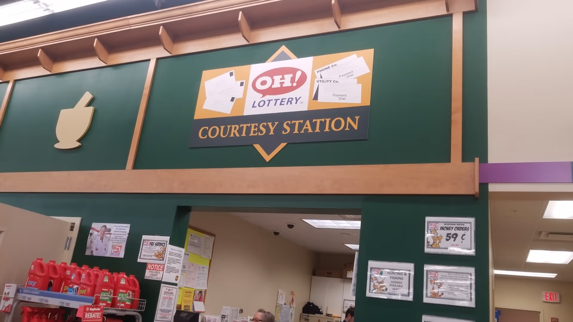 Inside a Discount Drug Mart, a green wall features a 'Courtesy Station' sign and lottery logo.
