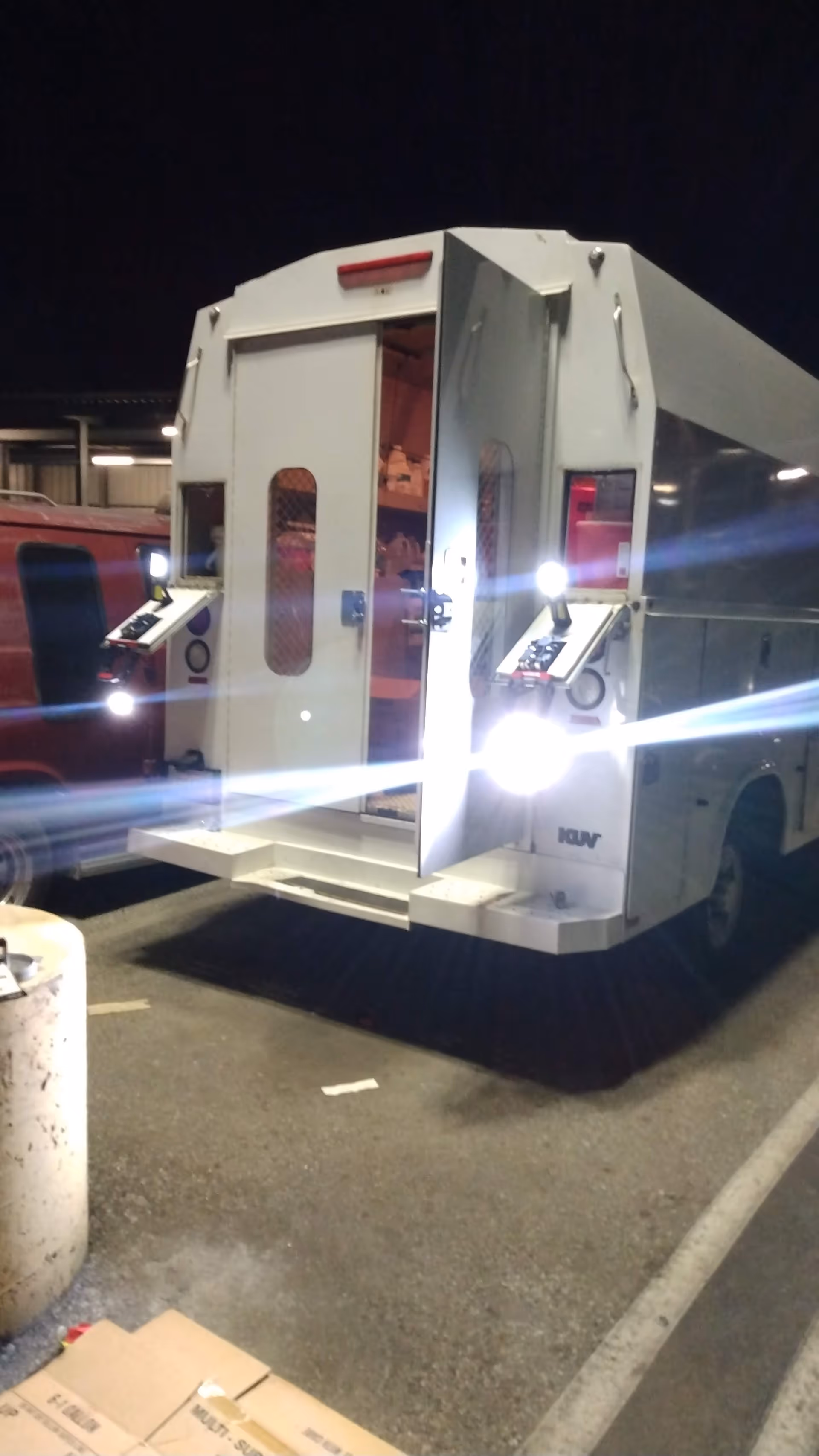 Rear of a white medical transport vehicle with open doors in a dim parking lot.