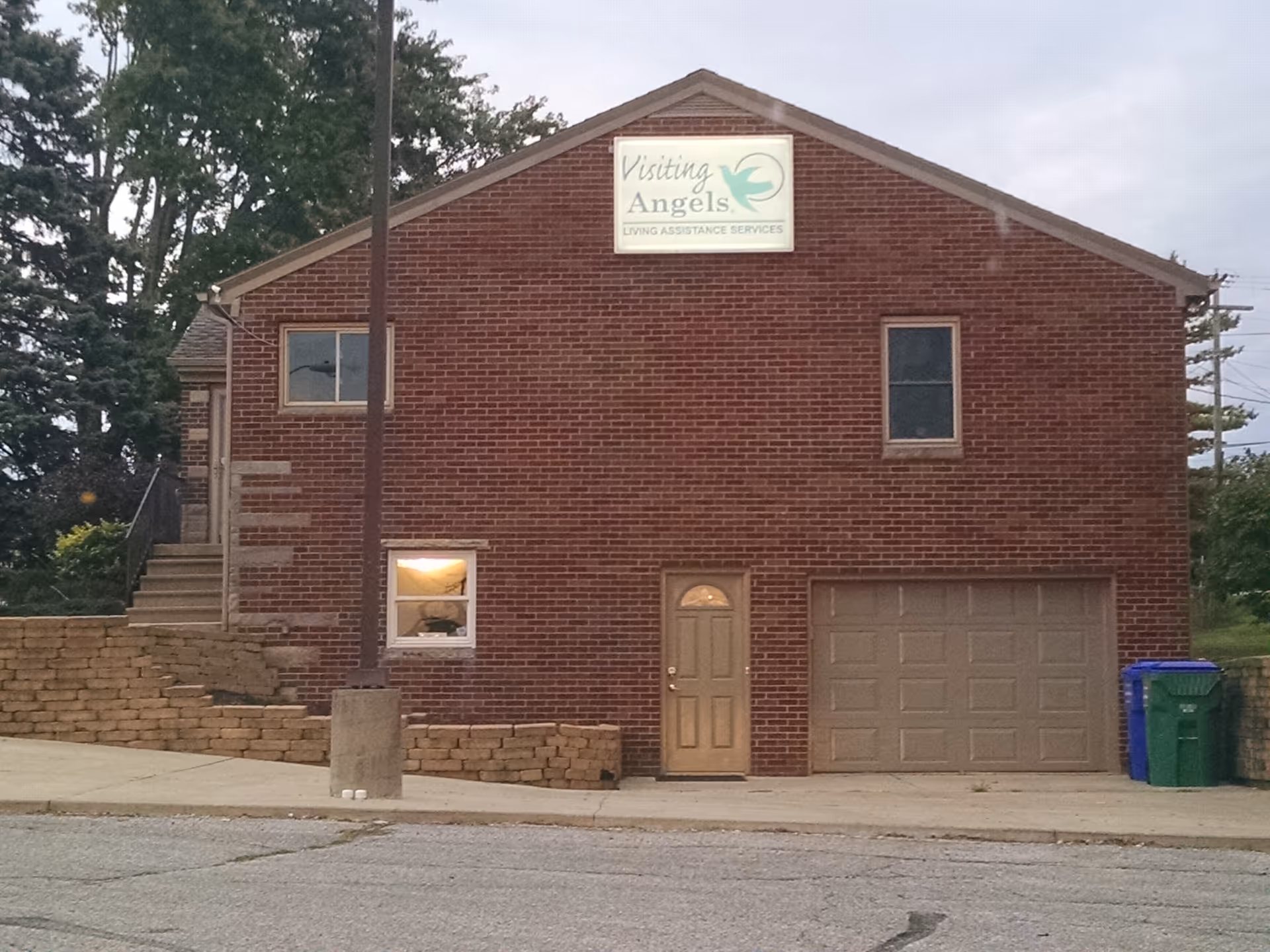 Two-story brick building with Visiting Angels sign, front door, garage, and sidewalk.