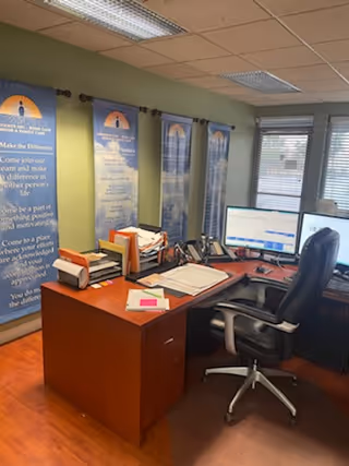 Office workspace with wooden desk, computer, stacks of documents, and wall banners.