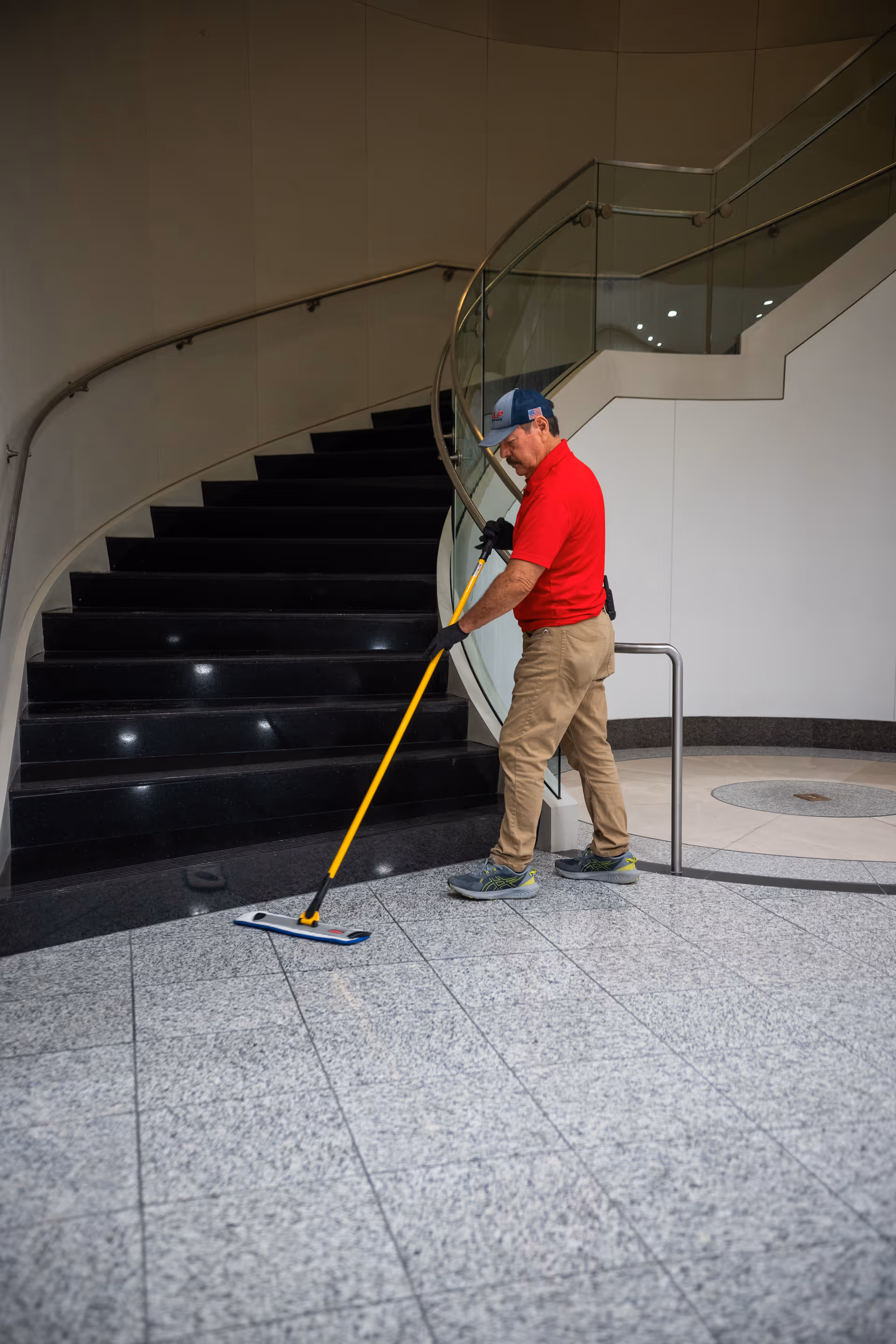 Maintenance worker mops the lobby floor beside a curved glass staircase.