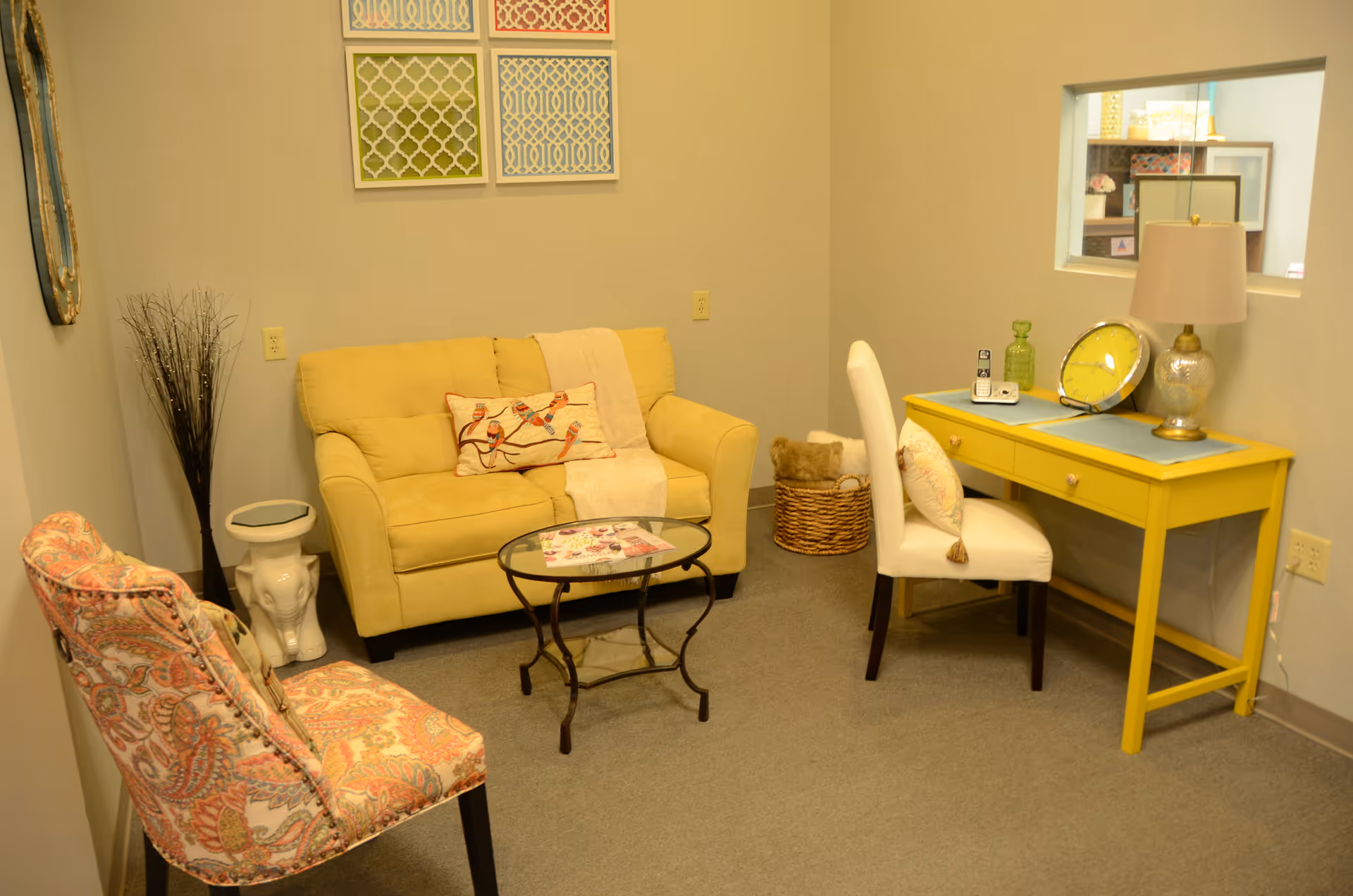 Bright lounge area with yellow desk, cream sofa, patterned chairs, and decorative wall art.