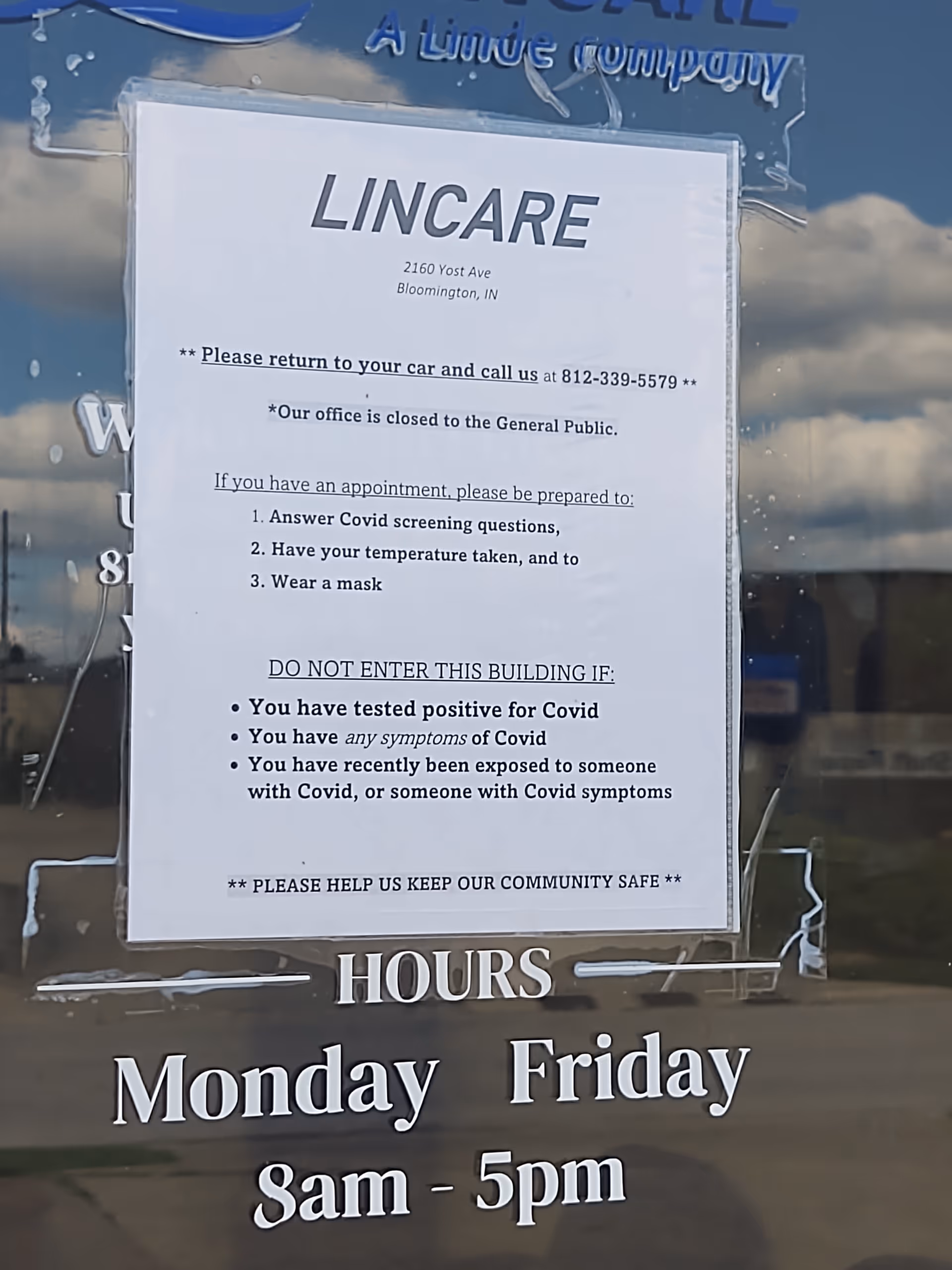Glass door with a LINCARE sign and a posted notice about hours and COVID guidelines.