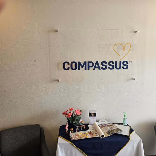 Interior lobby area with a Compassus sign, table, flowers, and brochures on display.