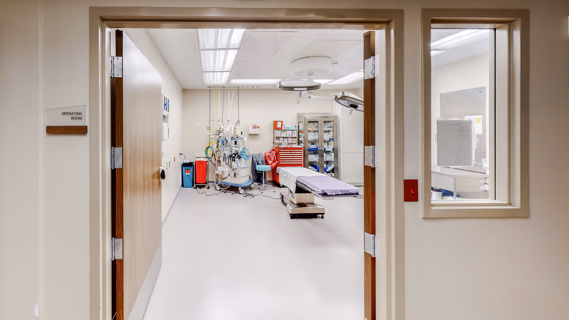 Doorway opens to an operating room with medical equipment and an adjustable operating table.