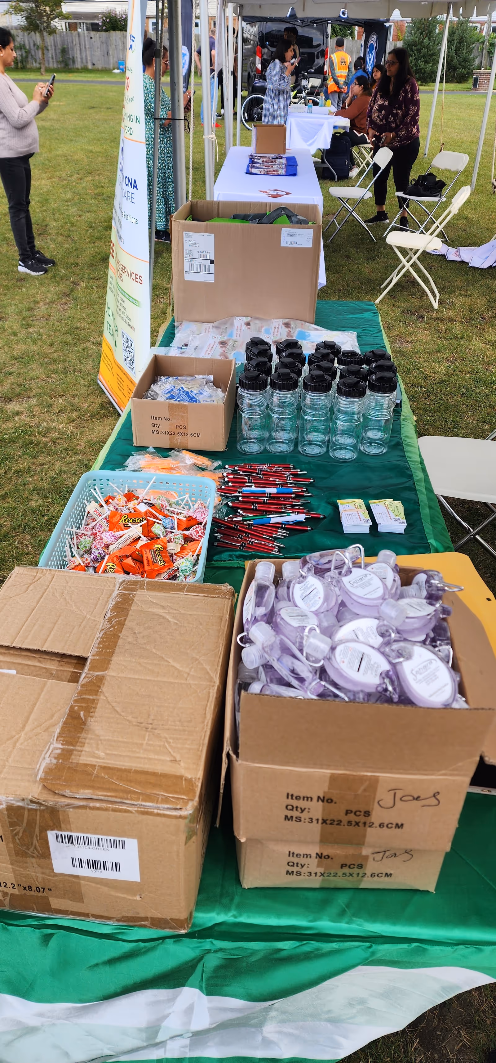 Outdoor Sahara Home Care event with tables, boxes, water bottles, and attendees under tents.