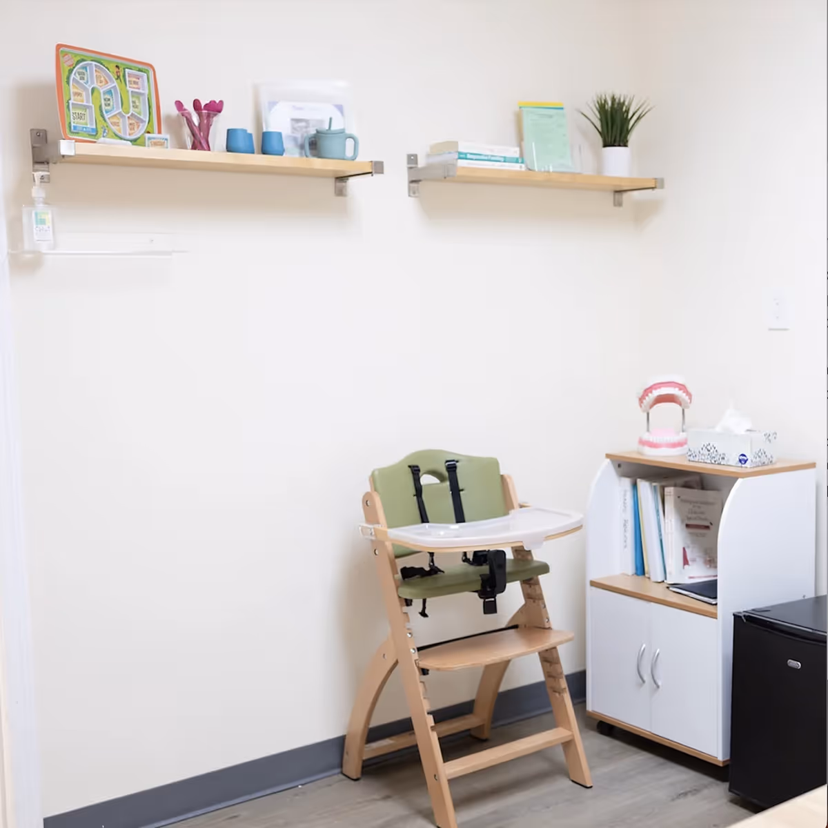 A small therapy room corner with a wooden high chair, books, and dental model.