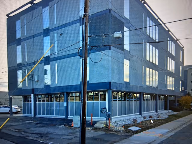 Three-story blue building exterior with large glass windows and a surrounding sidewalk.