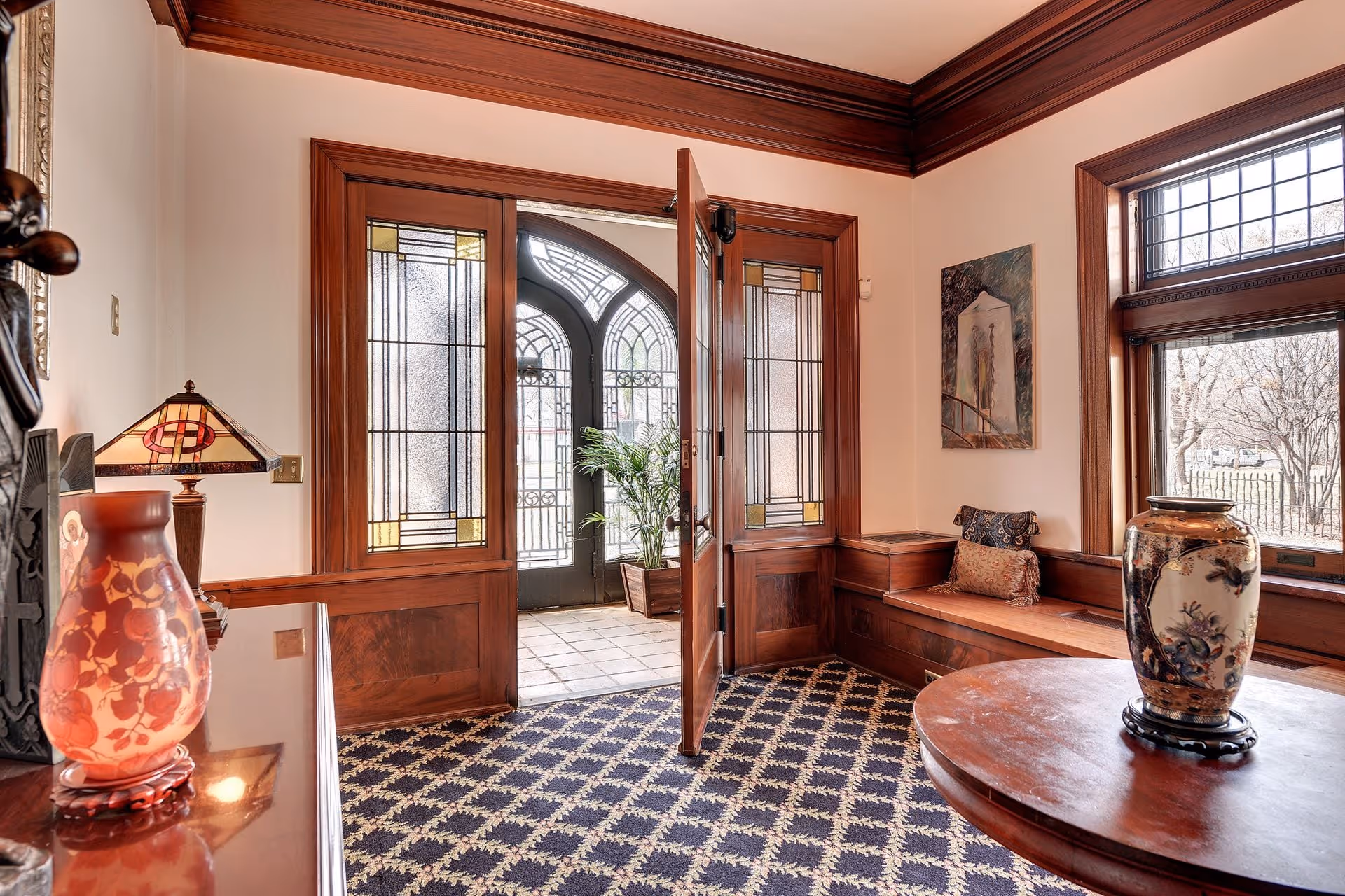 Warm wood-paneled foyer with glass doors, seating nook, and decorative vases.
