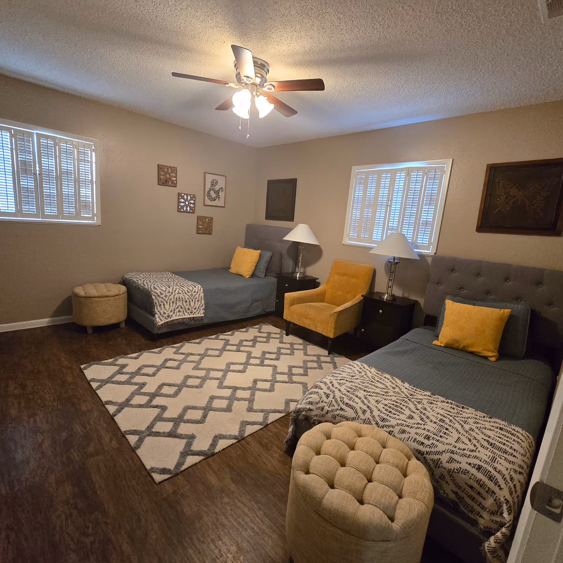 Two twin beds with blue bedding, yellow pillows, rug, chairs, and lamps in a bedroom.