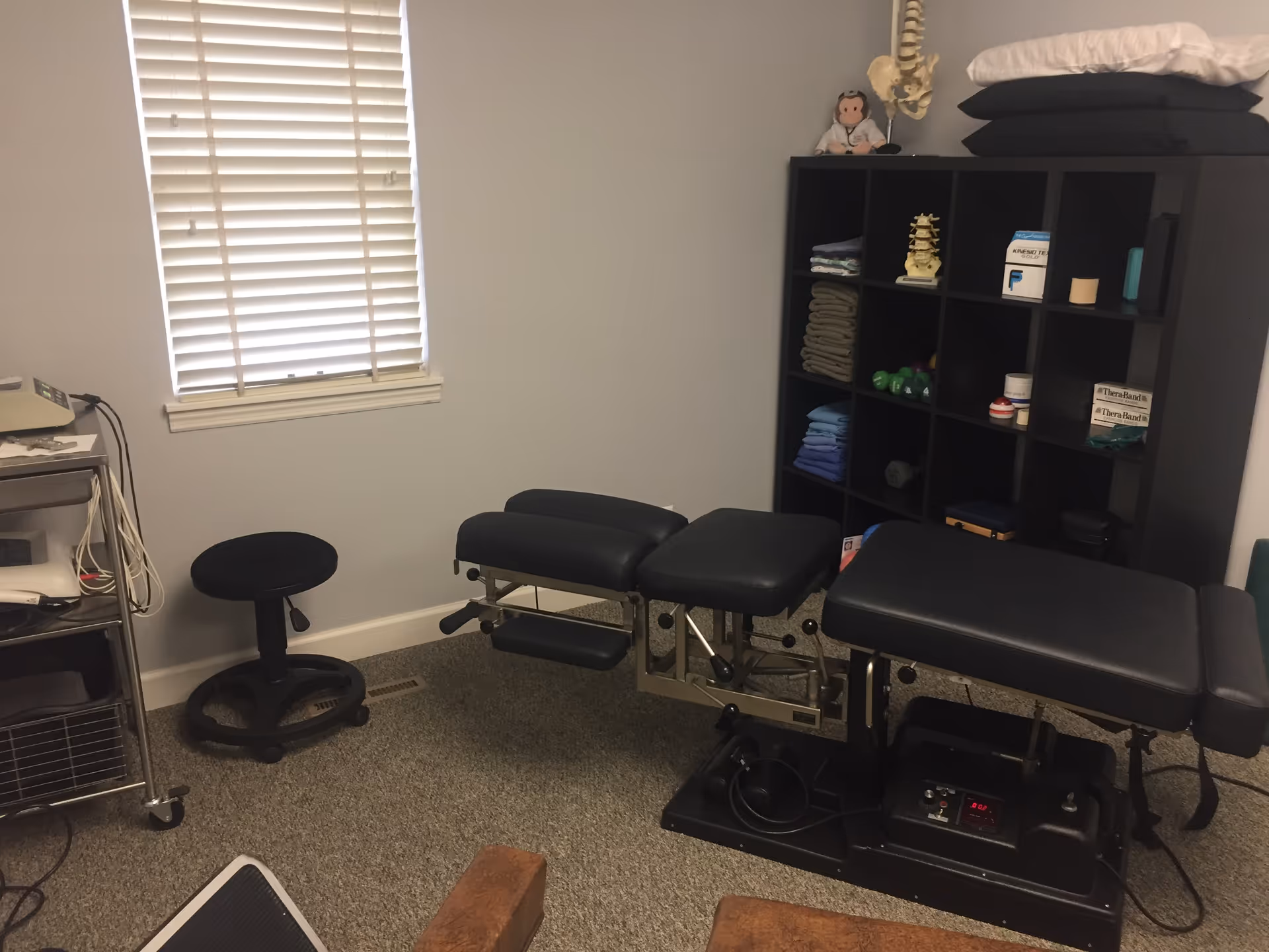 A chiropractic treatment room with a patient table, shelves, towels, and medical equipment.