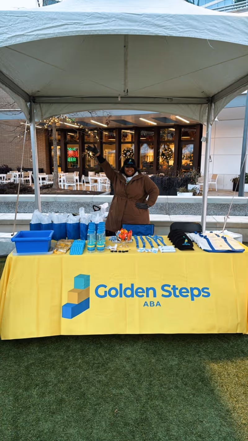 Outdoor tent booth featuring Golden Steps ABA table and staff member.