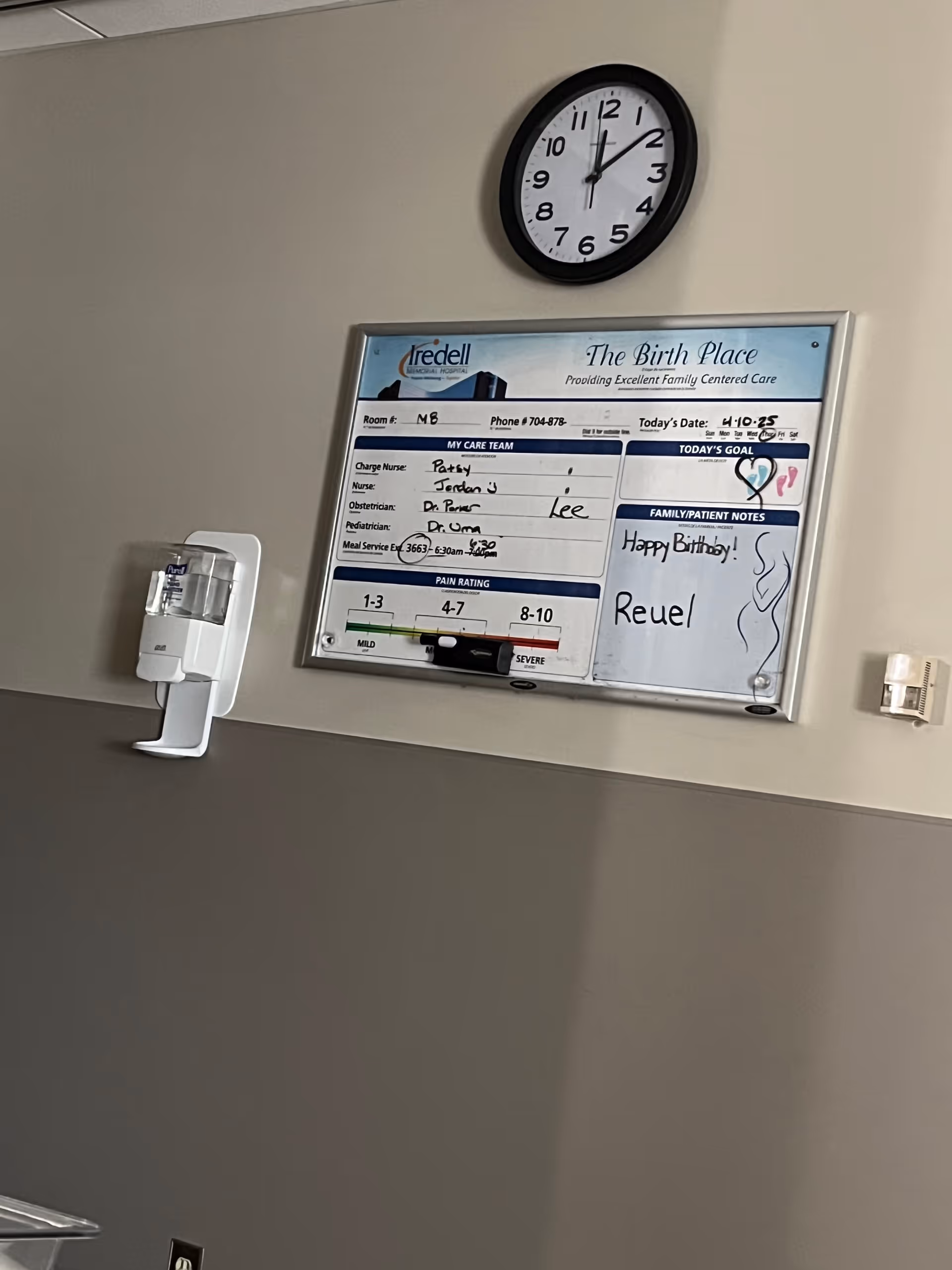 Interior hallway wall features clock, birth center board, and wall-mounted sanitizer dispenser.