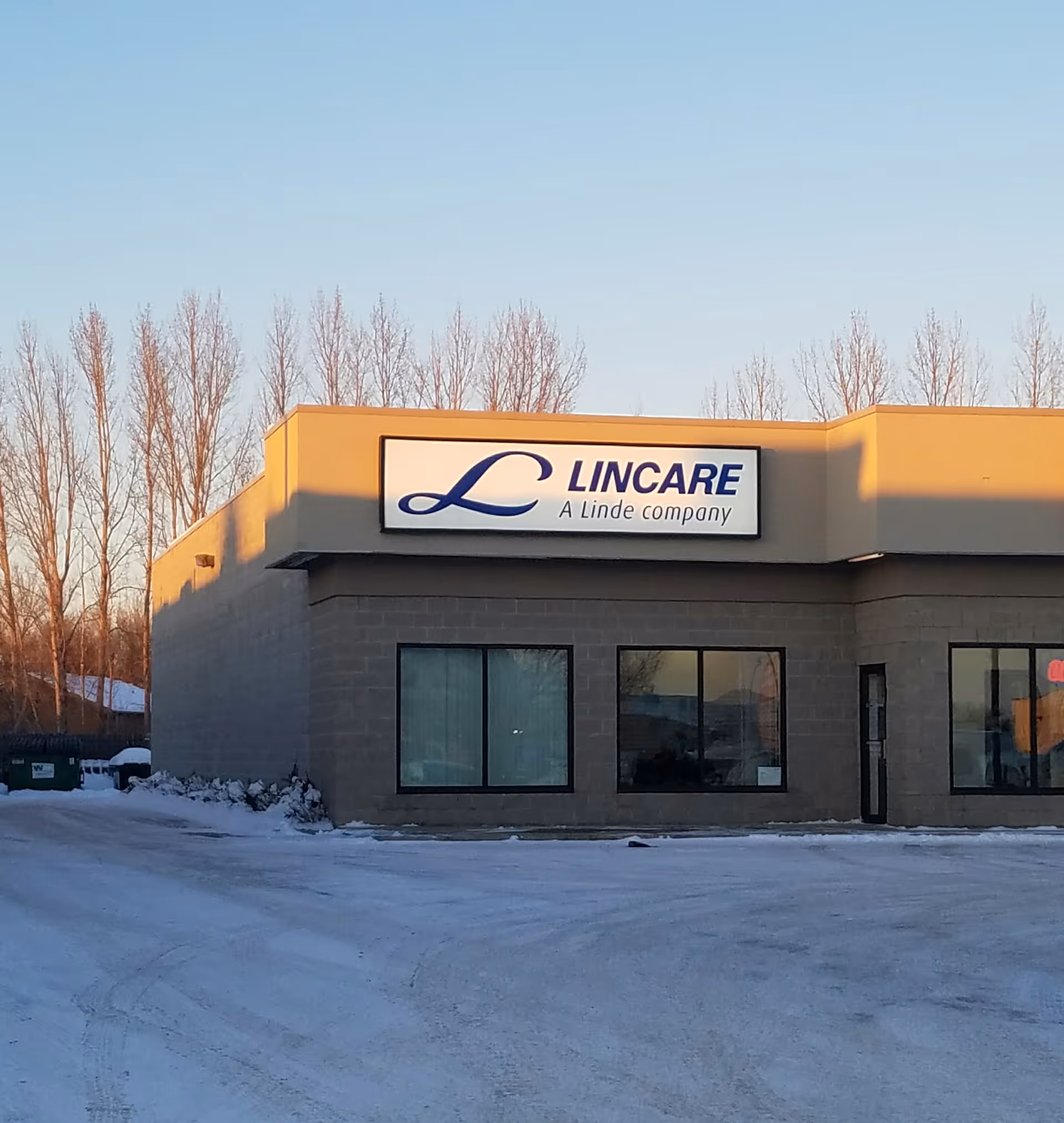 Exterior view of a LINCARE facility with a sign, snow, and a snow-covered parking lot.