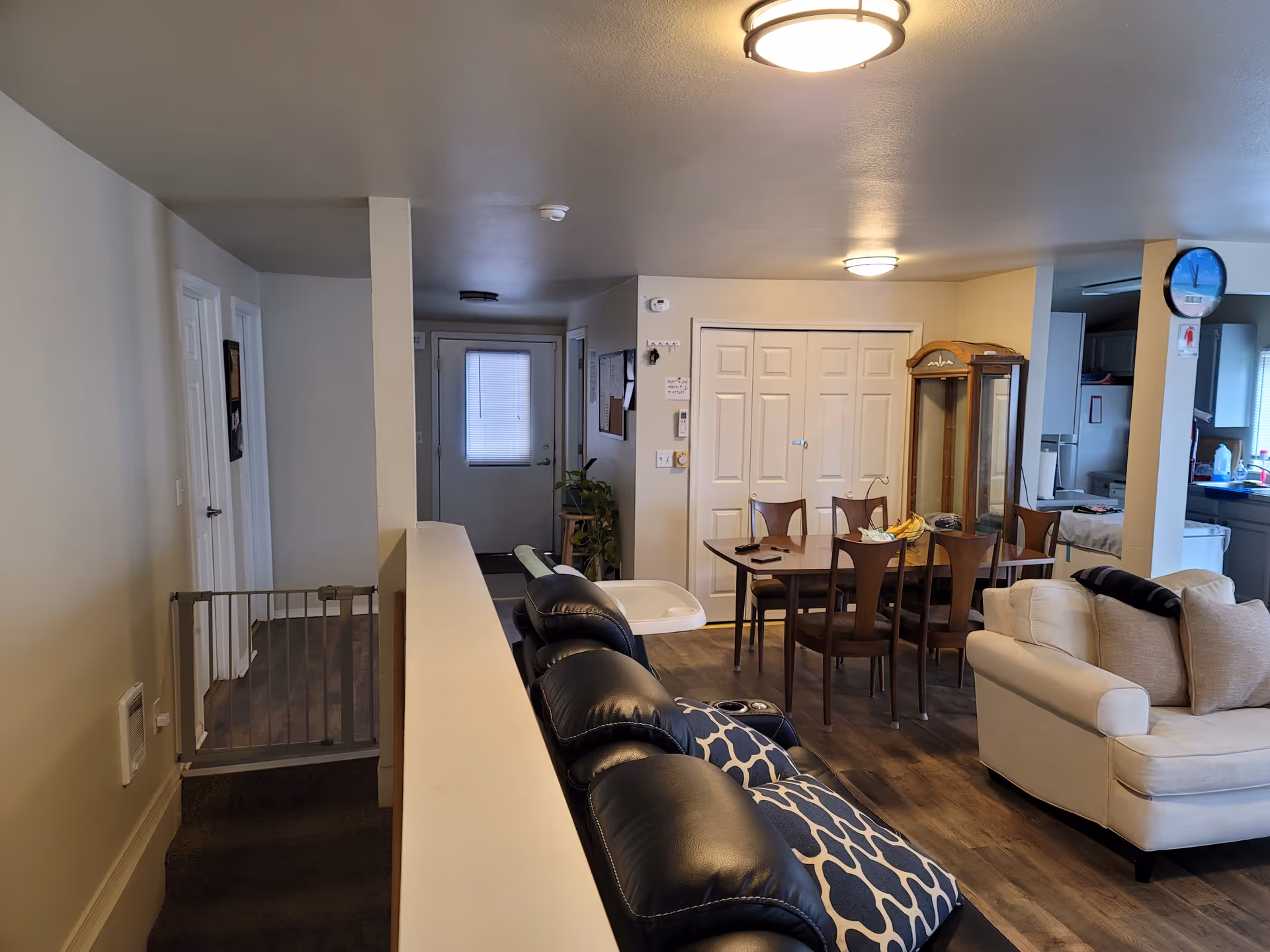 Open-concept living and dining area with cream sofa, wooden dining table, and visible kitchen.