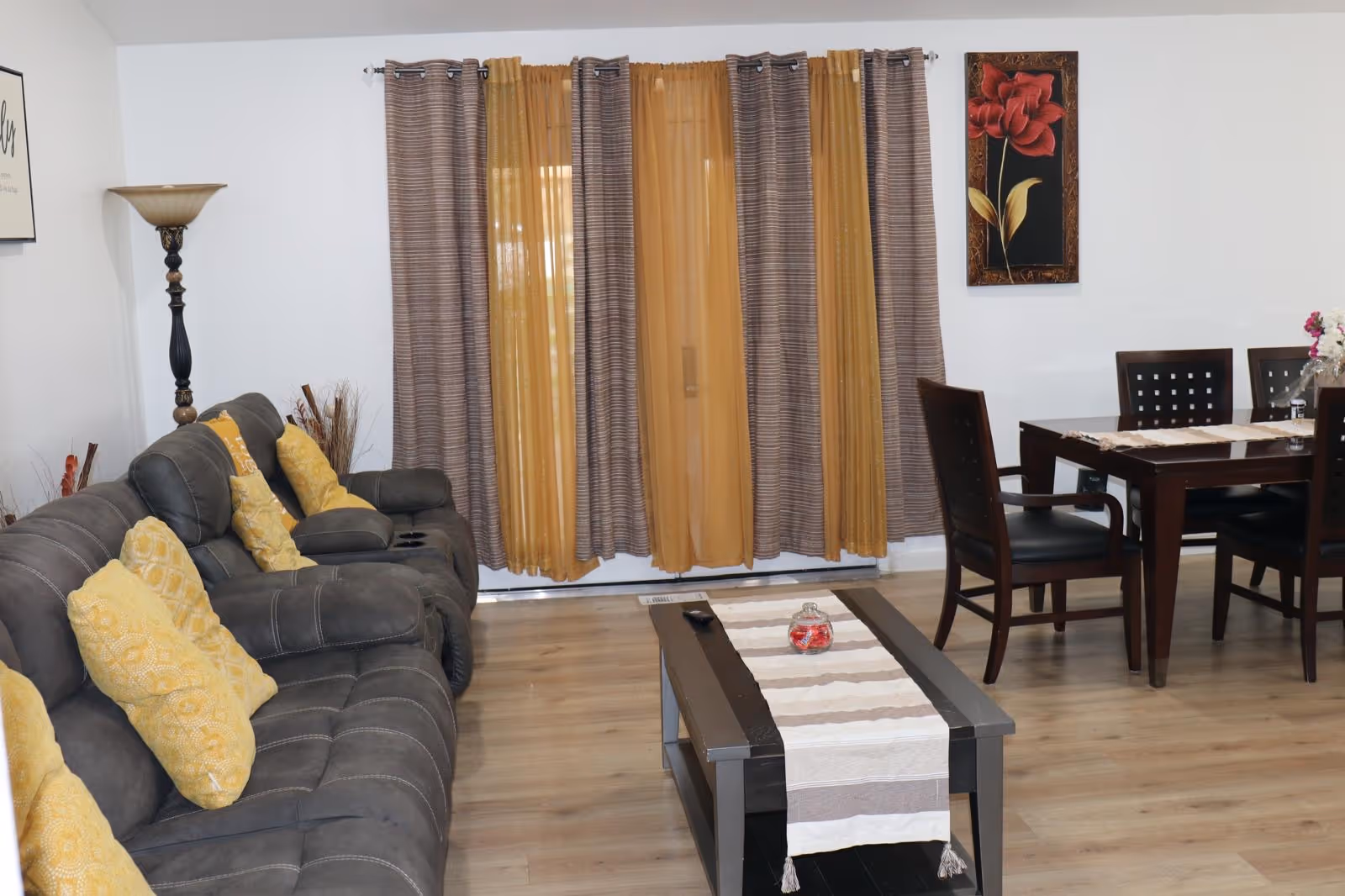 Cozy living room with gray sectional, yellow pillows, coffee table, dining area, and striped curtains.