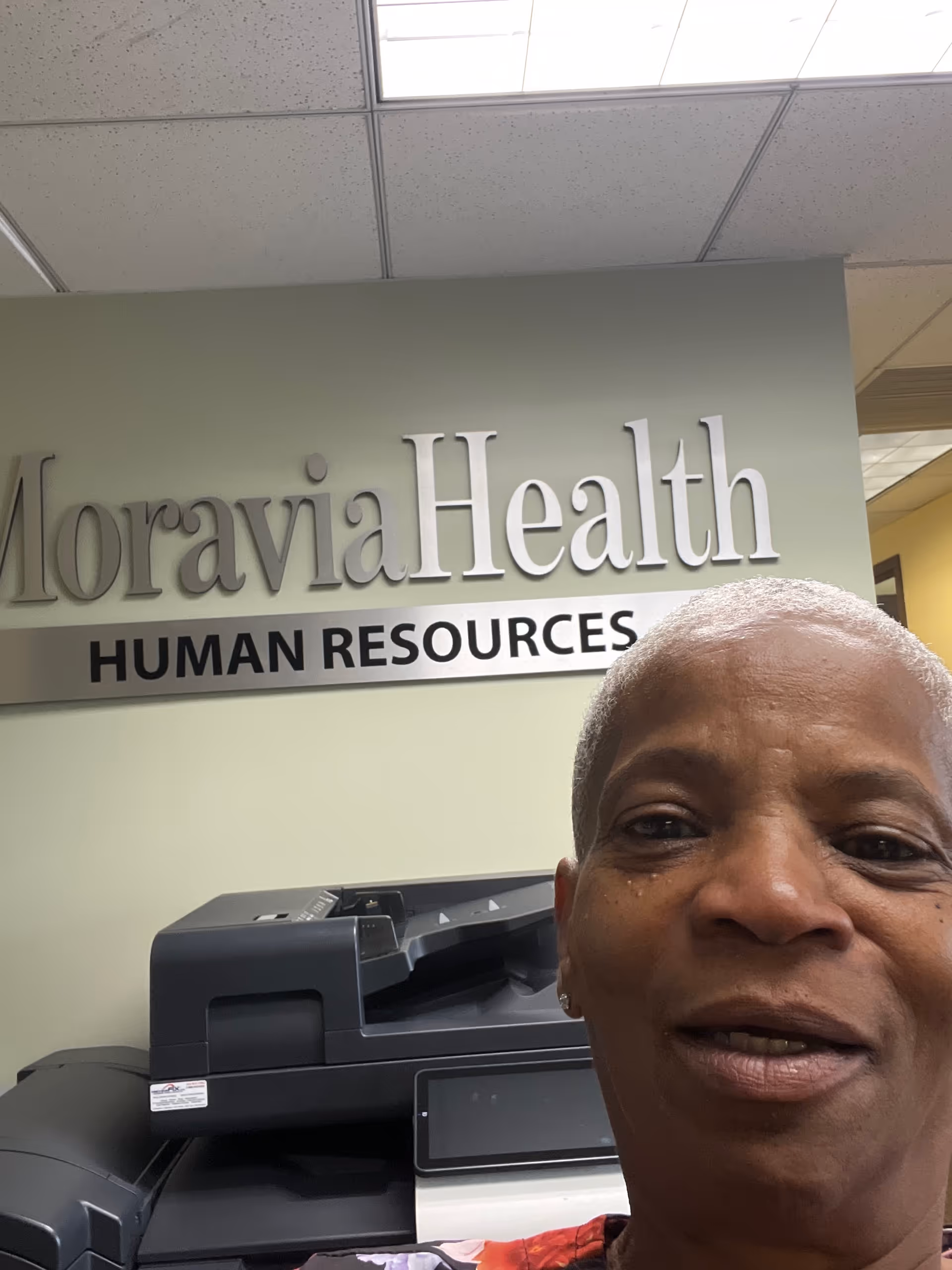 Partial selfie of a person in Moravia Health interior with a Human Resources sign.