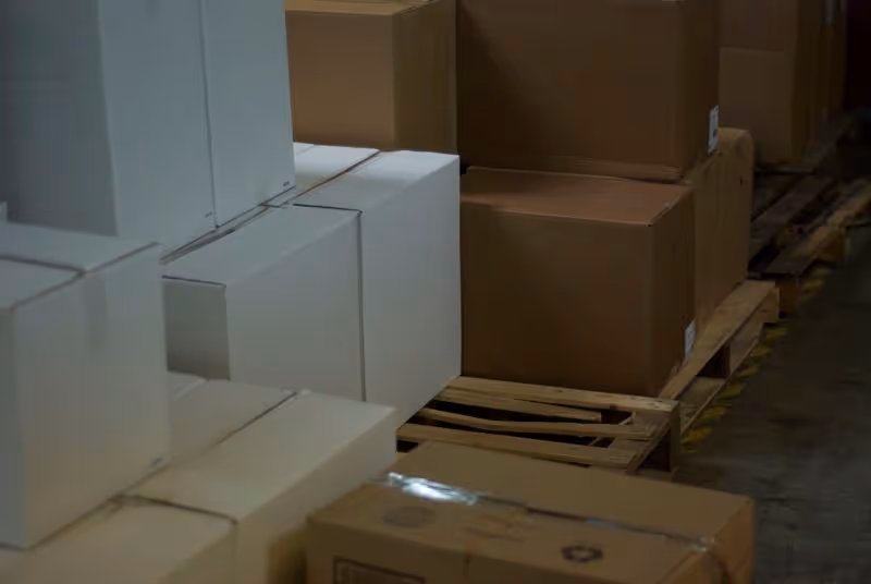 Stacks of white and brown cardboard boxes on pallets in a warehouse storage area.