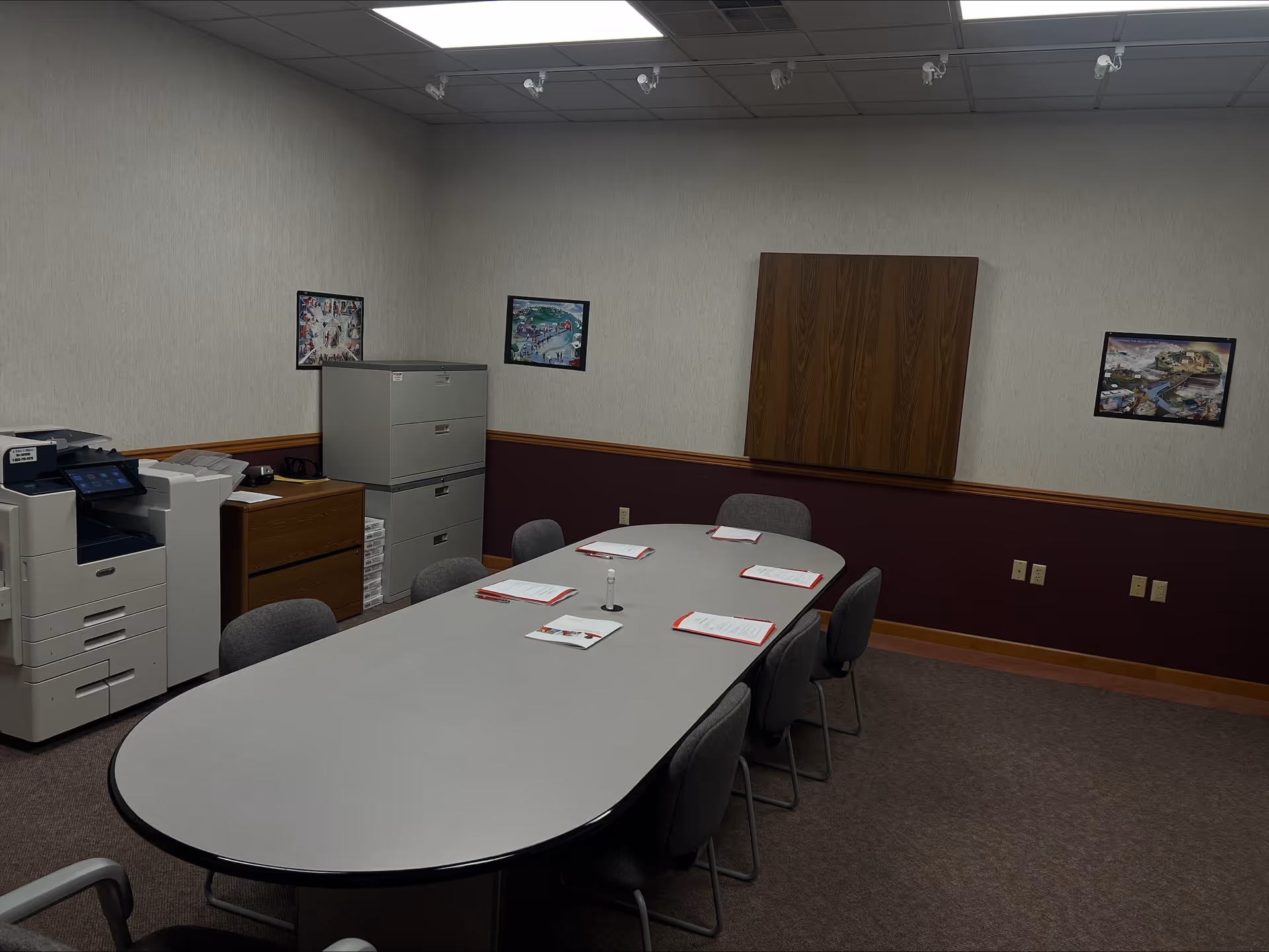 A conference room with an oval table, chairs, cabinets, and printers along the walls.