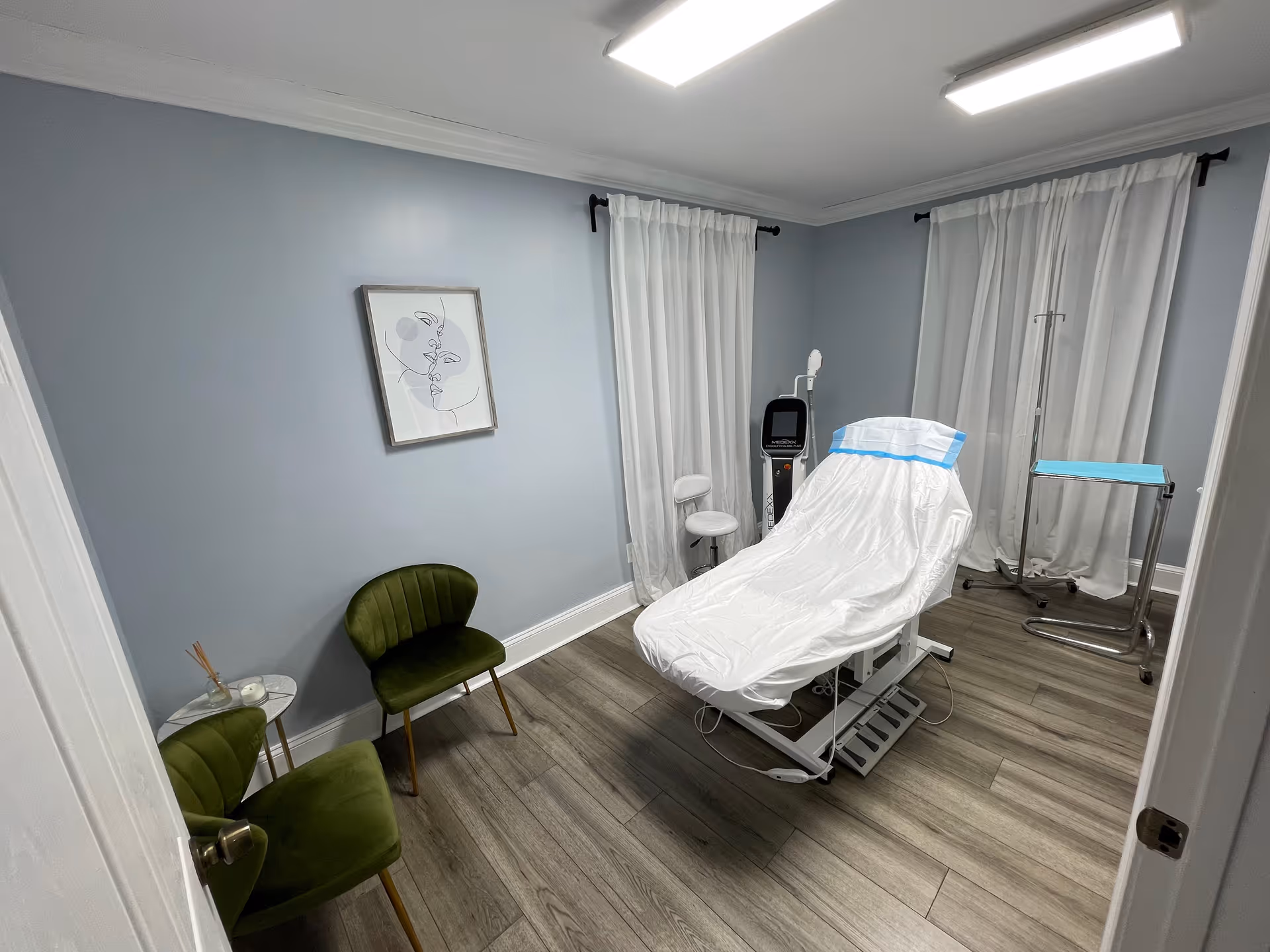 A medical treatment room with a white-covered examination bed, curtains, and modern equipment.