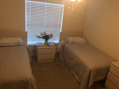 Two twin beds with a nightstand and flowers between, beige carpeted bedroom.