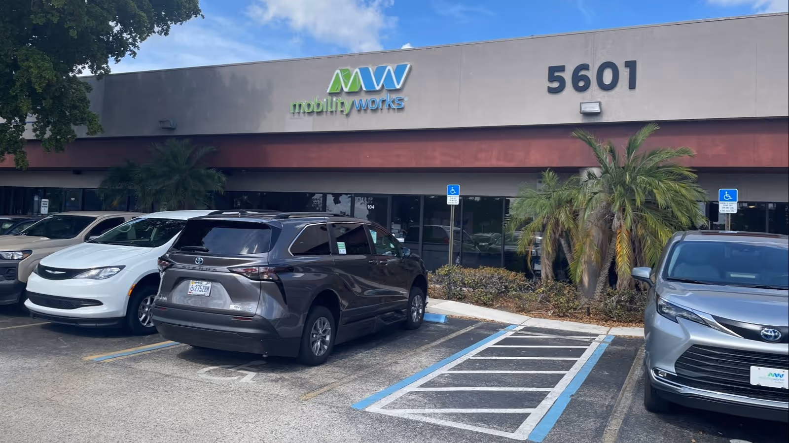 Facade of MobilityWorks storefront with parked cars and palm landscaping in front.