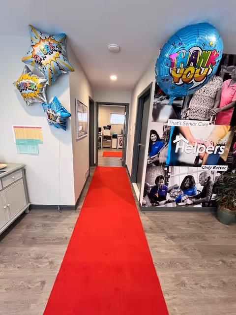 Hallway in a senior facility with a red carpet, balloons, and wall displays.