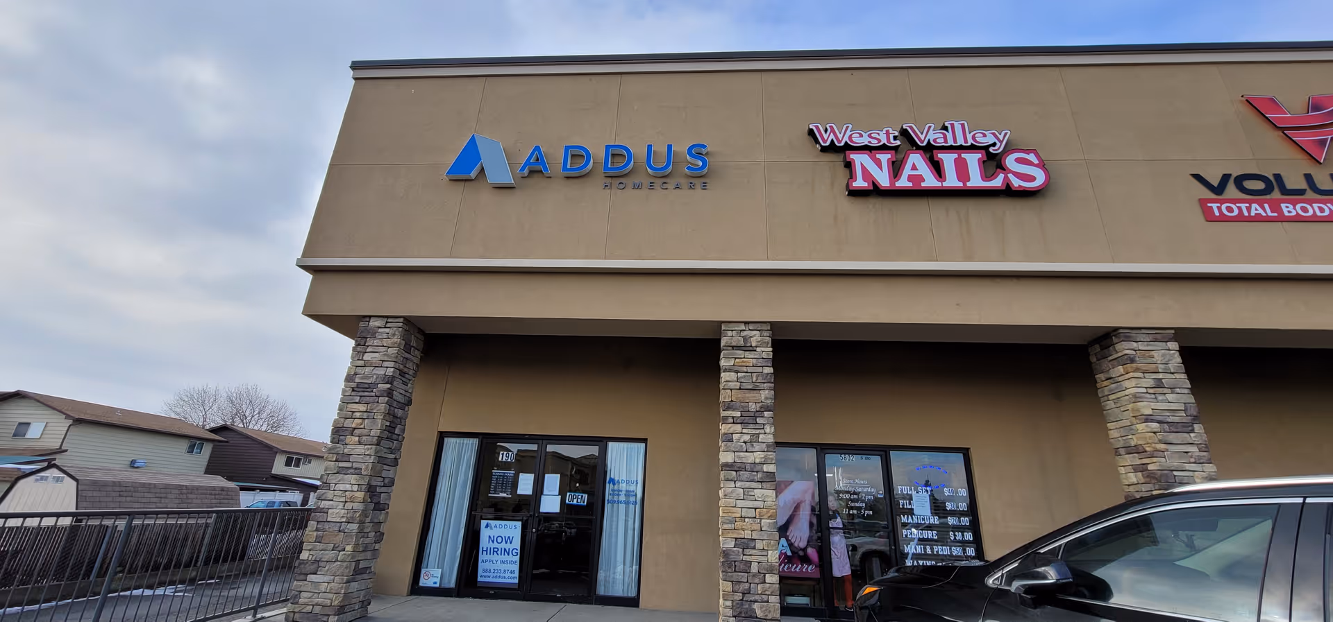 Exterior of a strip mall featuring Addus HomeCare signage and a neighboring nail salon storefront.