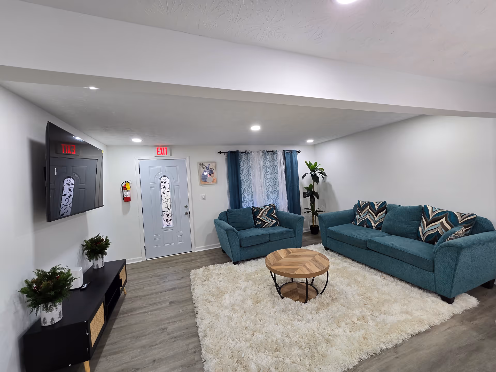 Cozy living room with teal couches, rug, coffee table, TV, and exit door.