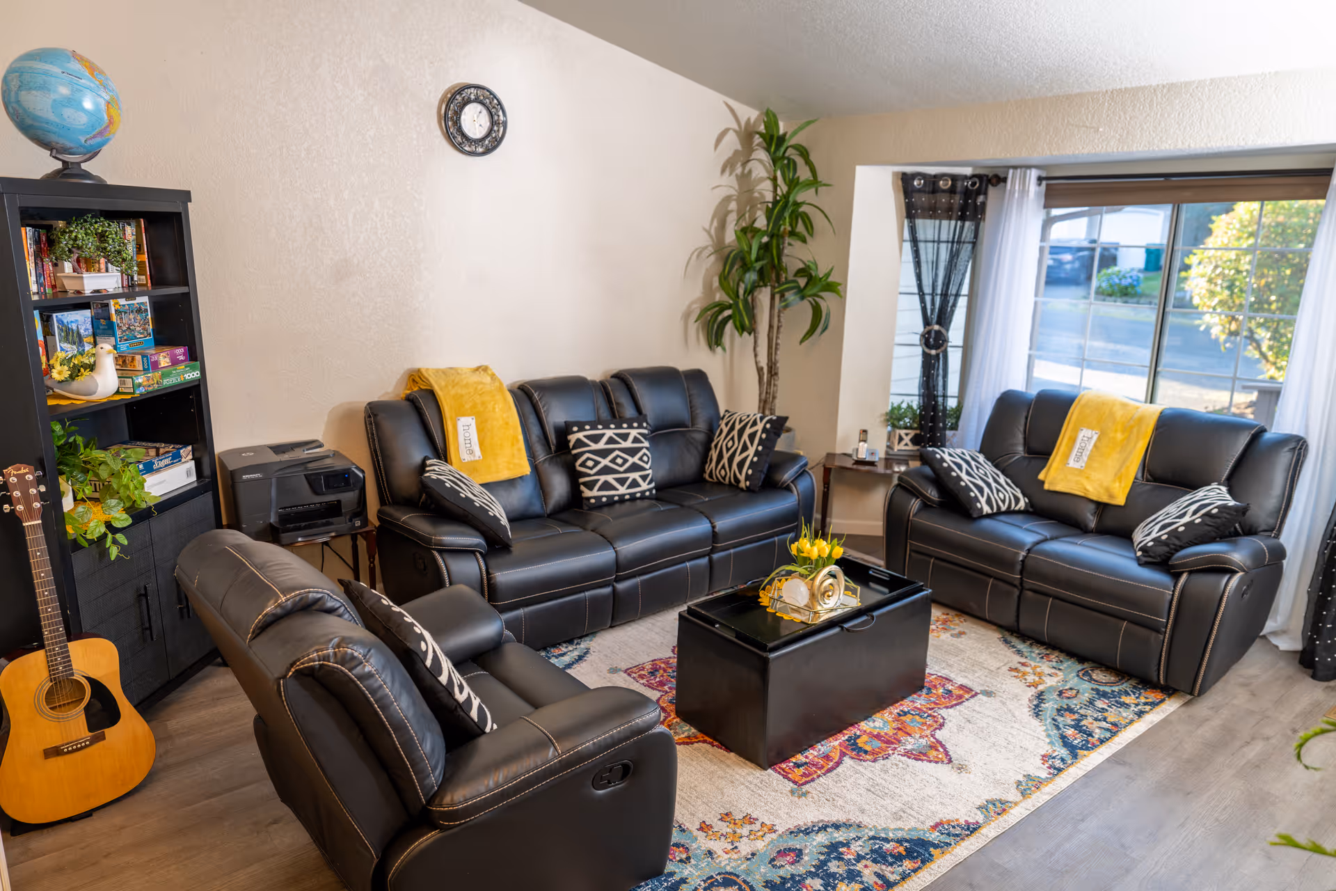 Cozy living room in a senior facility with black leather sofas, rug, and plants.